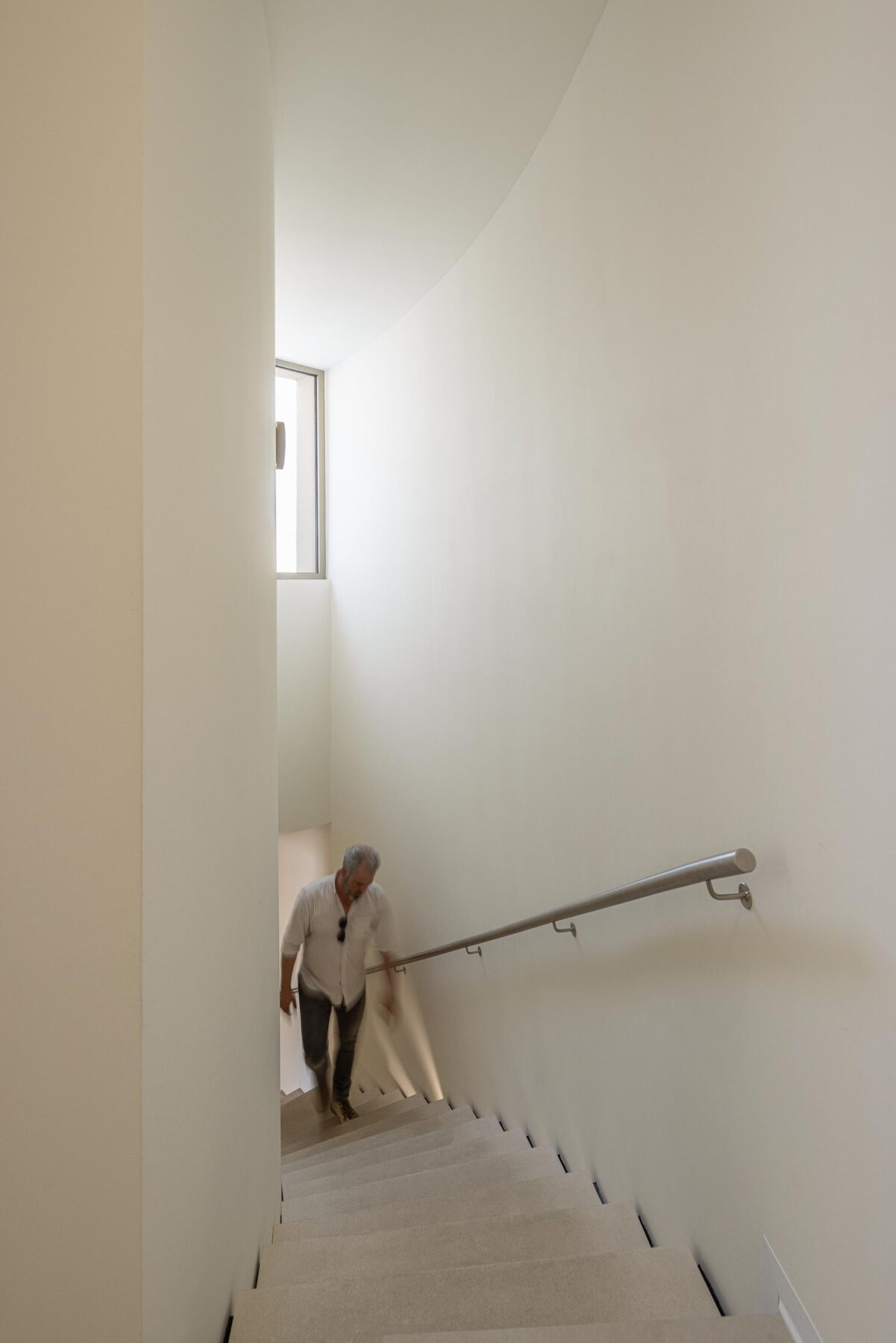 Escada curva com degraus em pedra clara e iluminação integrada, corrimão metálico e paredes brancas — Farmácia São João arquitectura Tsou Arquitectos fotografia Ivo Tavares
