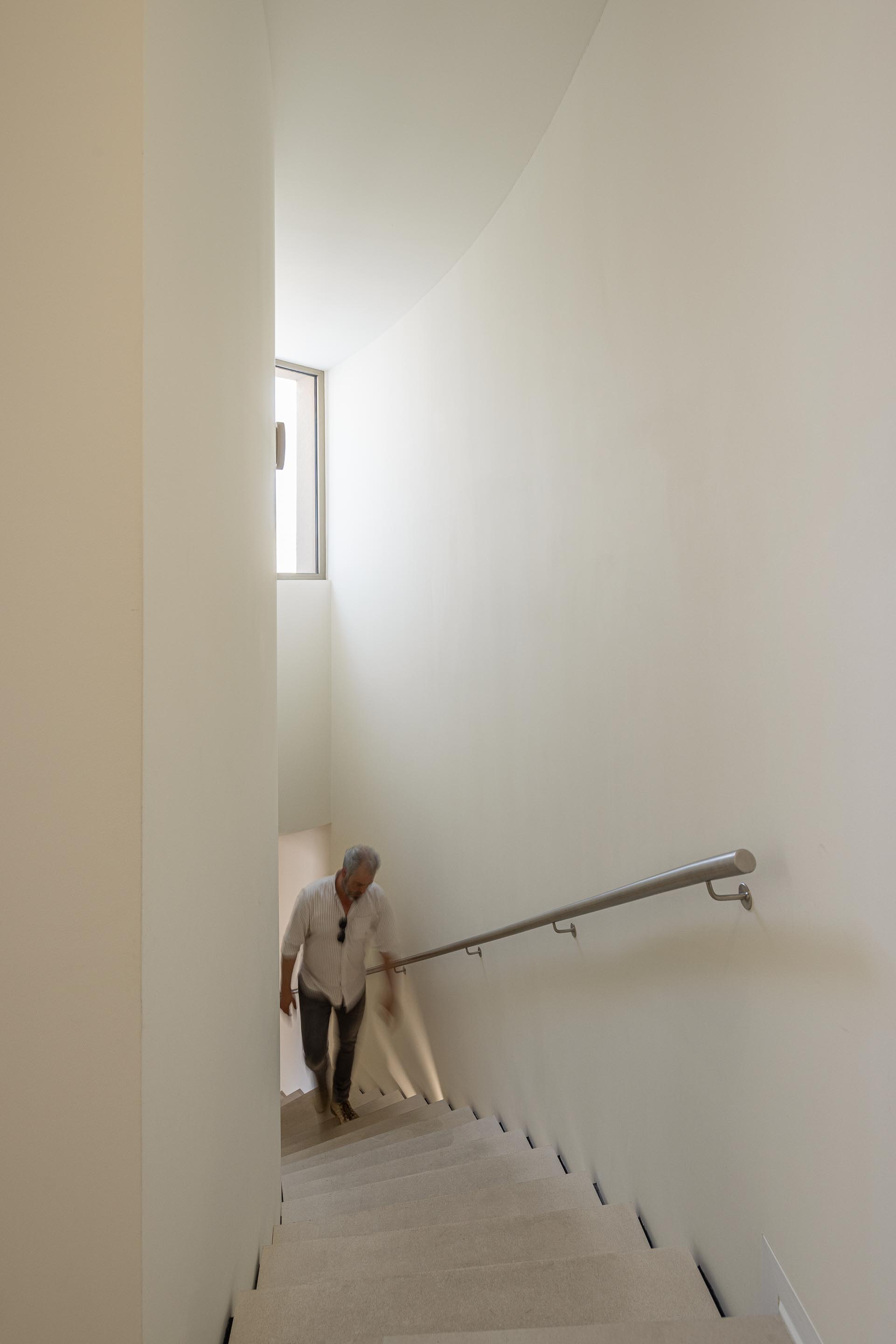 Escada curva com degraus em pedra clara e iluminação integrada, corrimão metálico e paredes brancas — Farmácia São João arquitectura Tsou Arquitectos fotografia Ivo Tavares