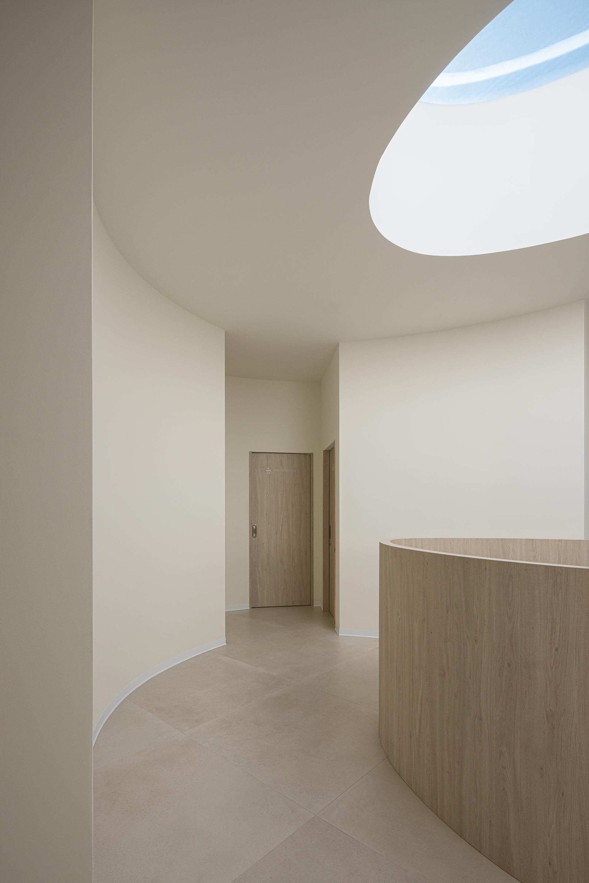 Escada curva em pedra clara com corrimão metálico, paredes brancas e luz natural de vão superior — Farmácia São João arquitectura Tsou Arquitectos fotografia Ivo Tavares