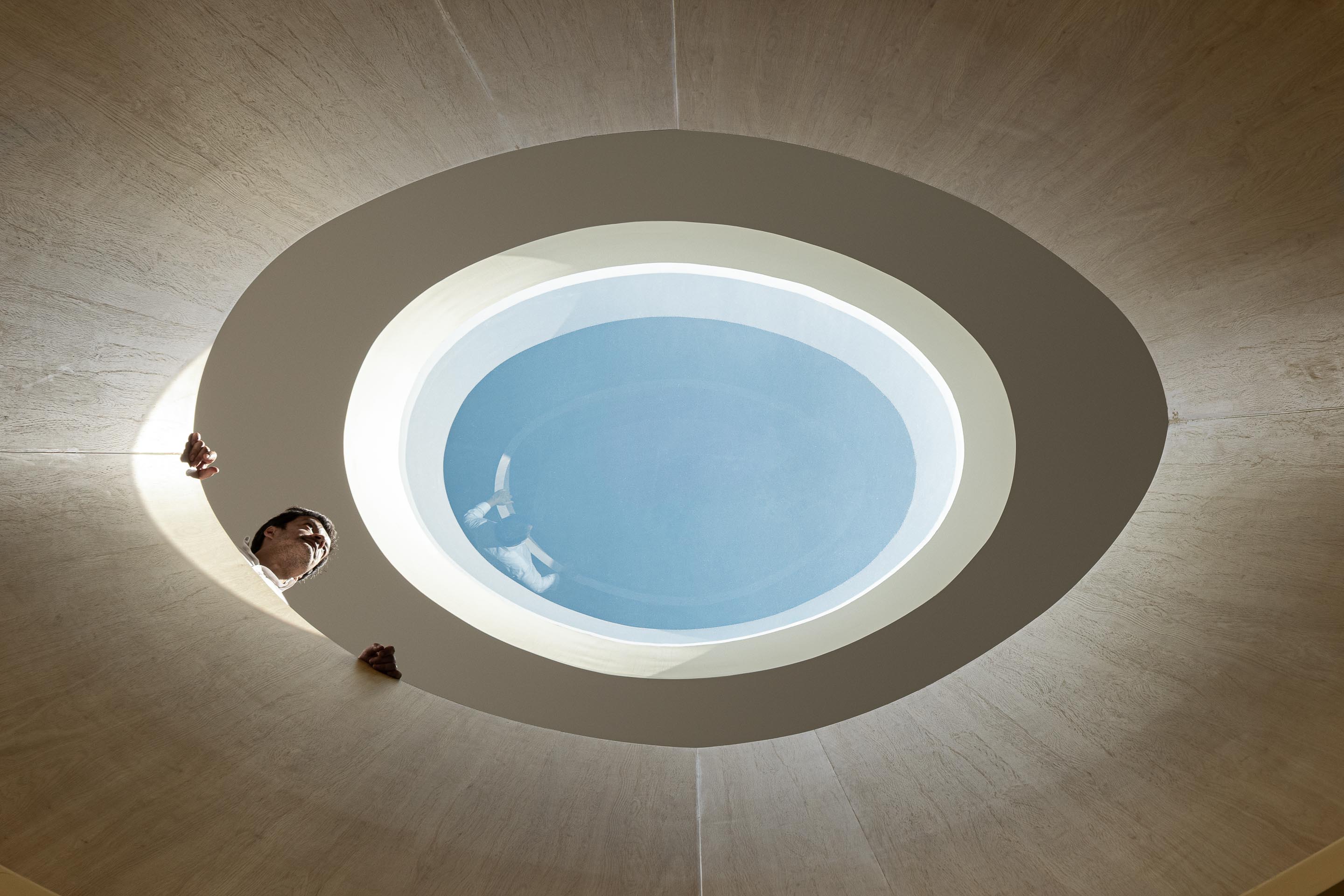 Corredor curvo com balcão em carvalho e pavimento cerâmico, iluminado por clarabóia oval no teto branco — Farmácia São João arquitectura Tsou Arquitectos fotografia Ivo Tavares