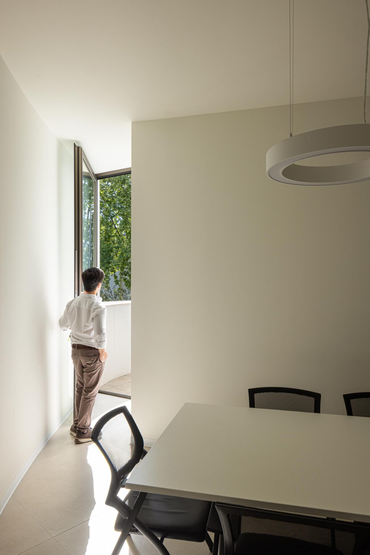 Sala de reuniões com paredes brancas, mesa retangular e candeeiros circulares suspensos, sob luz suave — Farmácia São João arquitectura Tsou Arquitectos fotografia Ivo Tavares