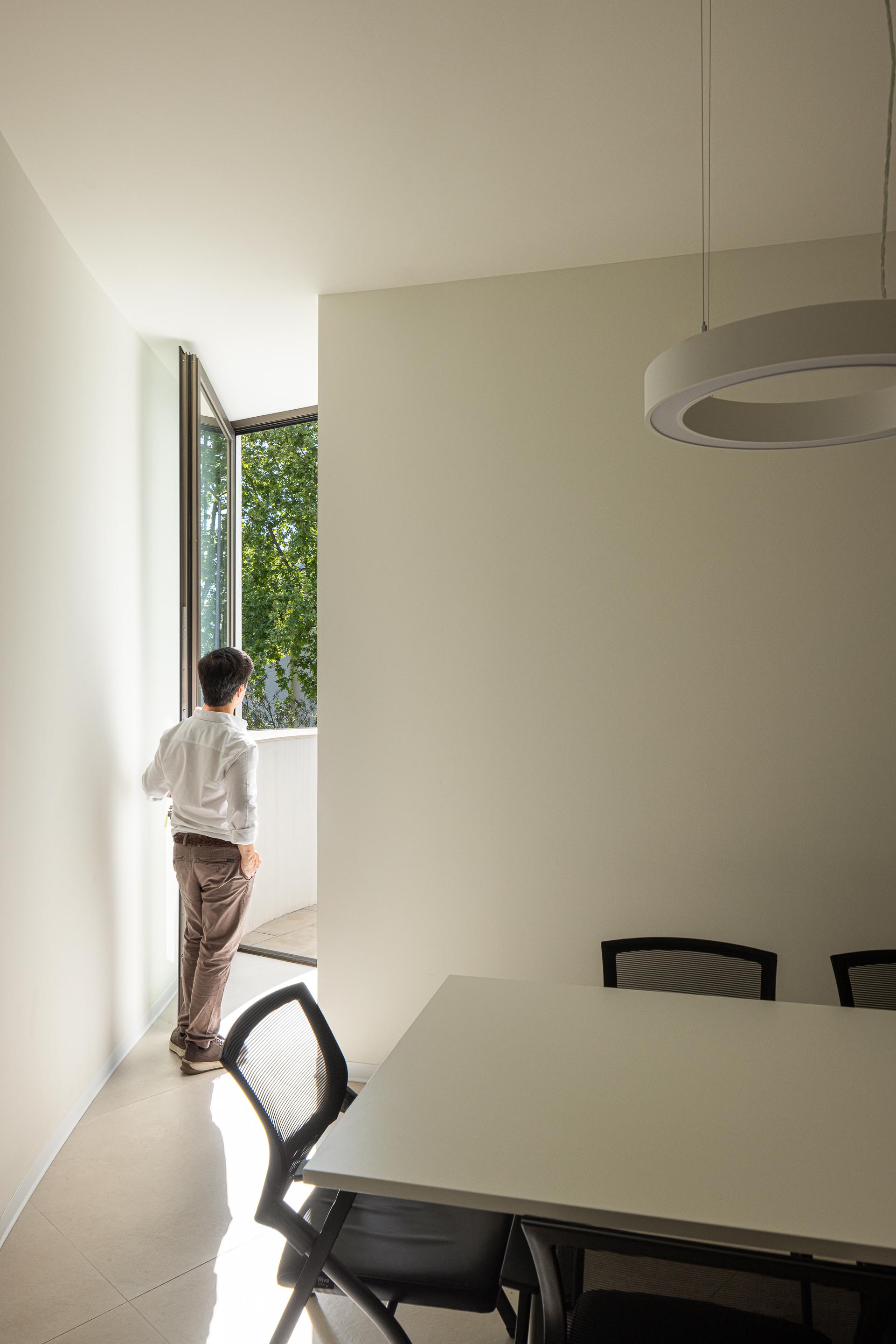 Sala de reuniões com paredes brancas, mesa retangular e candeeiros circulares suspensos, sob luz suave — Farmácia São João arquitectura Tsou Arquitectos fotografia Ivo Tavares