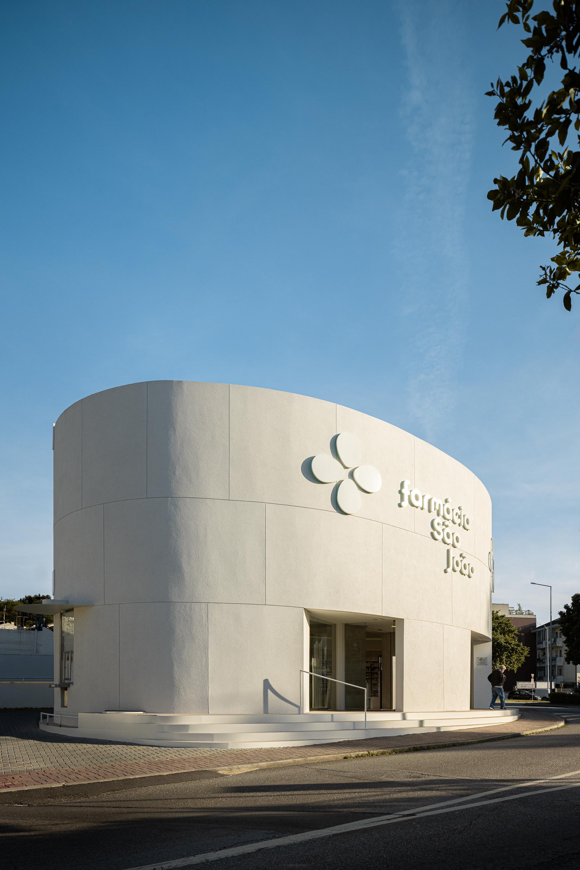 Fachada curva em EPS projetado branco com sinalética em relevo e reclamo luminoso, e degraus curvos — Farmácia São João arquitectura Tsou Arquitectos fotografia Ivo Tavares