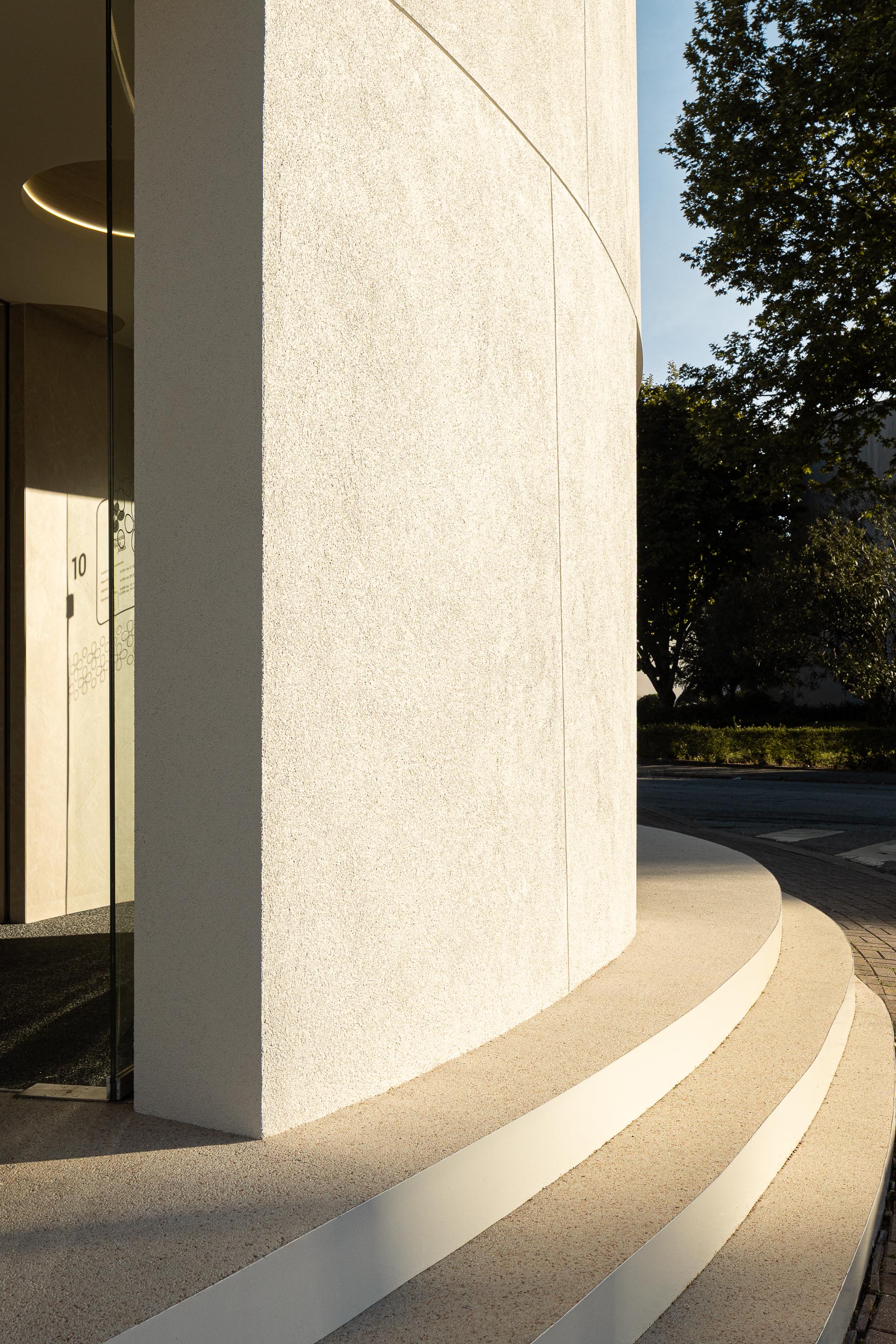 Entrada com degraus em mármore de Estremoz jateado, corrimão branco e porta envidraçada na fachada curva — Farmácia São João arquitectura Tsou Arquitectos fotografia Ivo Tavares