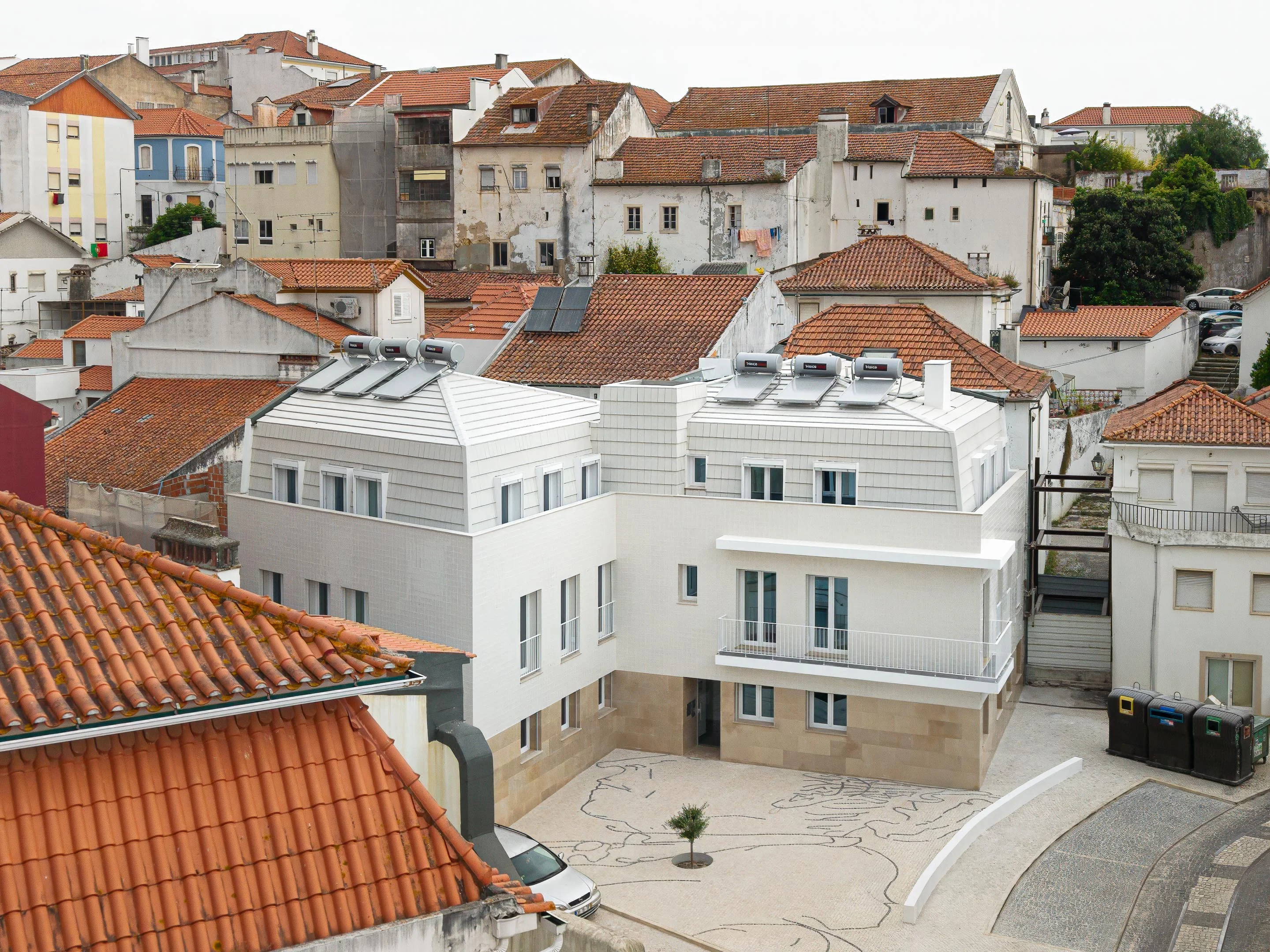 Fachada em azulejo branco e cobertura amansardada em telha plana. Base em pedra calc&aacute;ria e pavimento em cal&ccedil;ada portuguesa com desenho &mdash; Edif&iacute;cio Actriz Virginia arquitectura Adarq &ndash; Andr&eacute; David Arquitecto fotografia Ivo Tavares