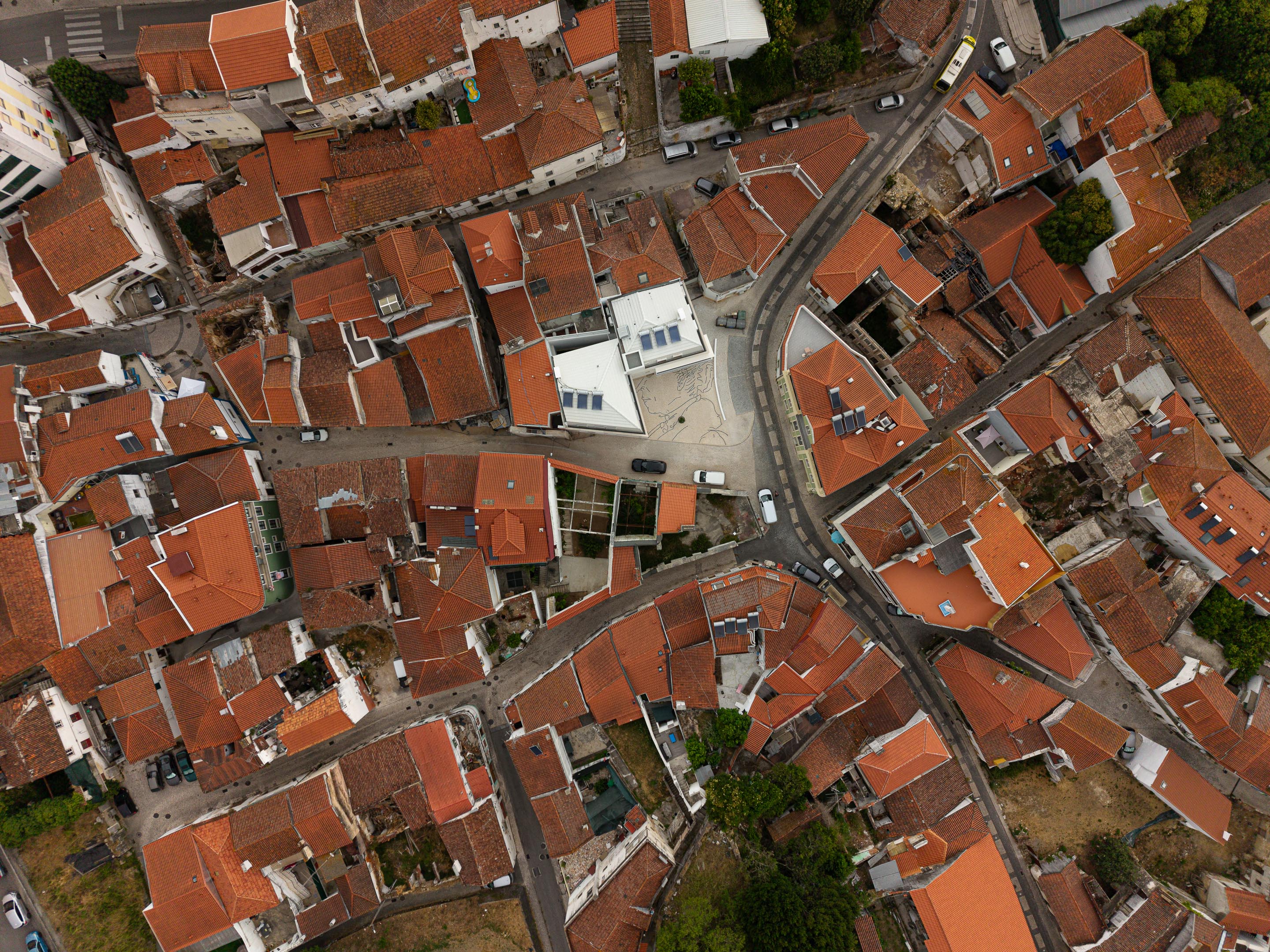 Vista aérea do edifício branco integrado no tecido urbano, rodeado por coberturas de telha cerâmica tradicional — Edifício Actriz Virginia arquitectura Adarq – André David Arquitecto fotografia Ivo Tavares