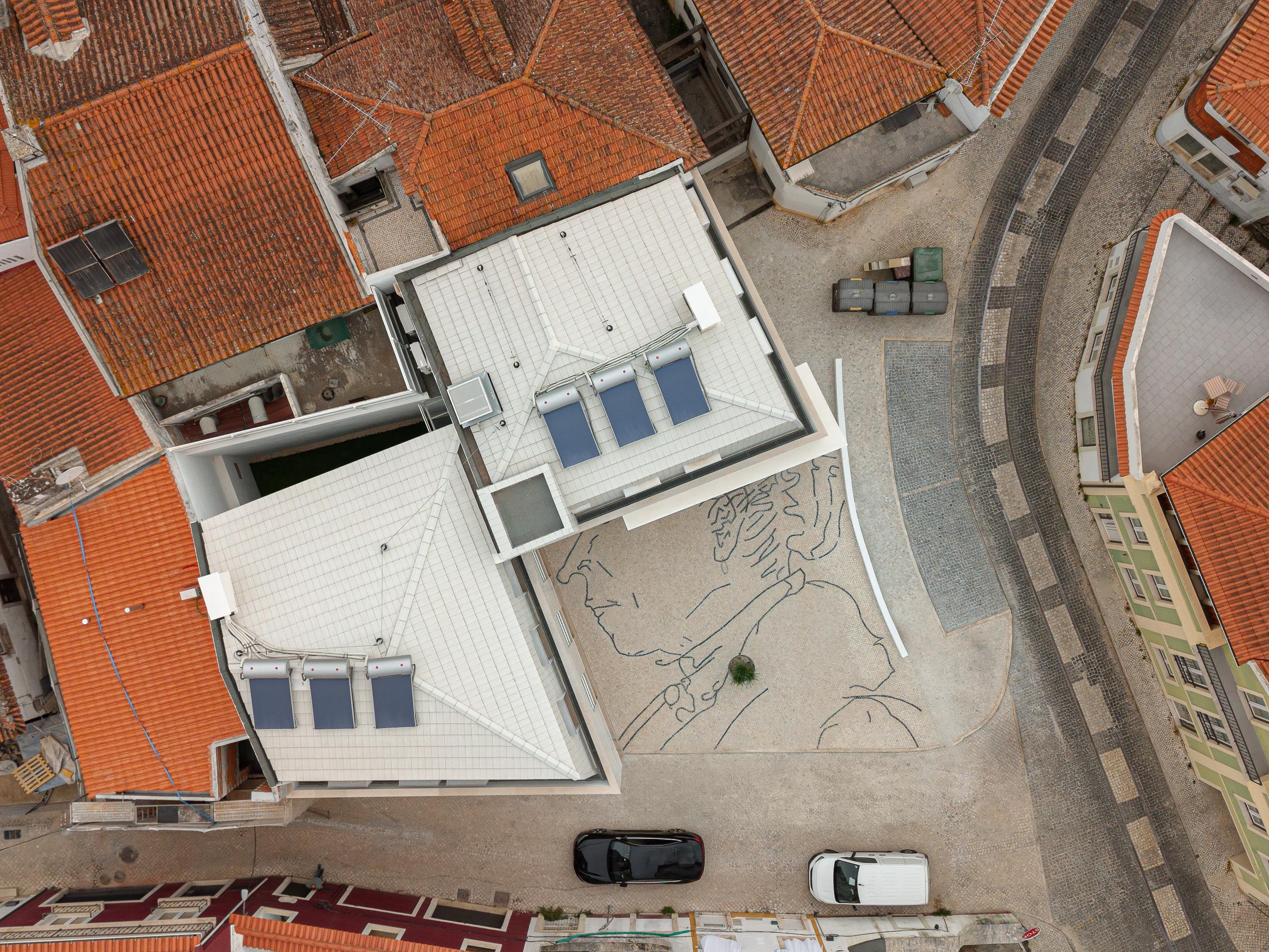Cobertura amansardada em telha plana branca com painéis solares. Pavimento em calçada portuguesa clara com desenho abstrato em basalto — Edifício Actriz Virginia arquitectura Adarq – André David Arquitecto fotografia Ivo Tavares