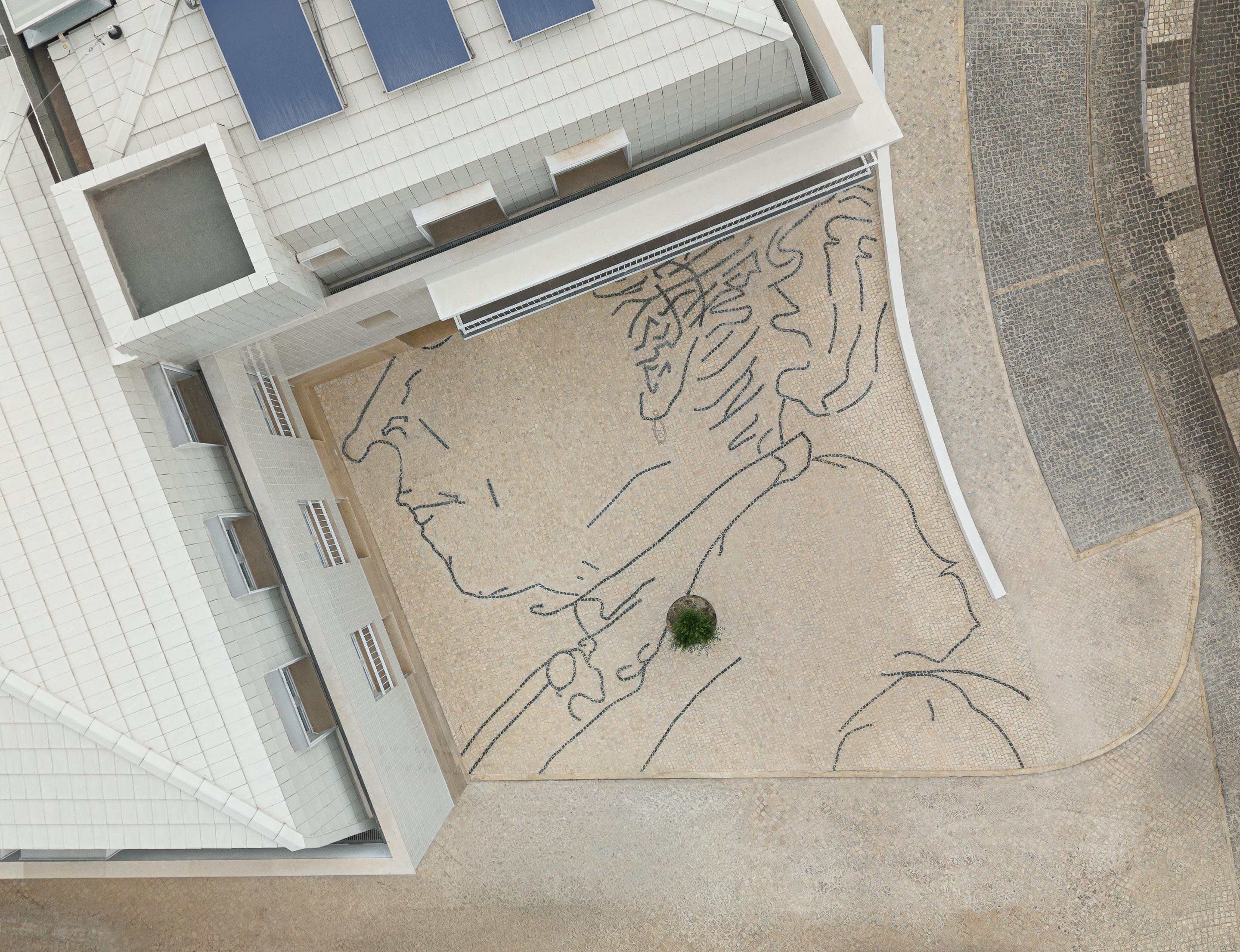 Detalhe do pavimento em calçada portuguesa com desenho de perfil em basalto escuro sobre pedra calcária clara, com uma pequena árvore — Edifício Actriz Virginia arquitectura Adarq – André David Arquitecto fotografia Ivo Tavares