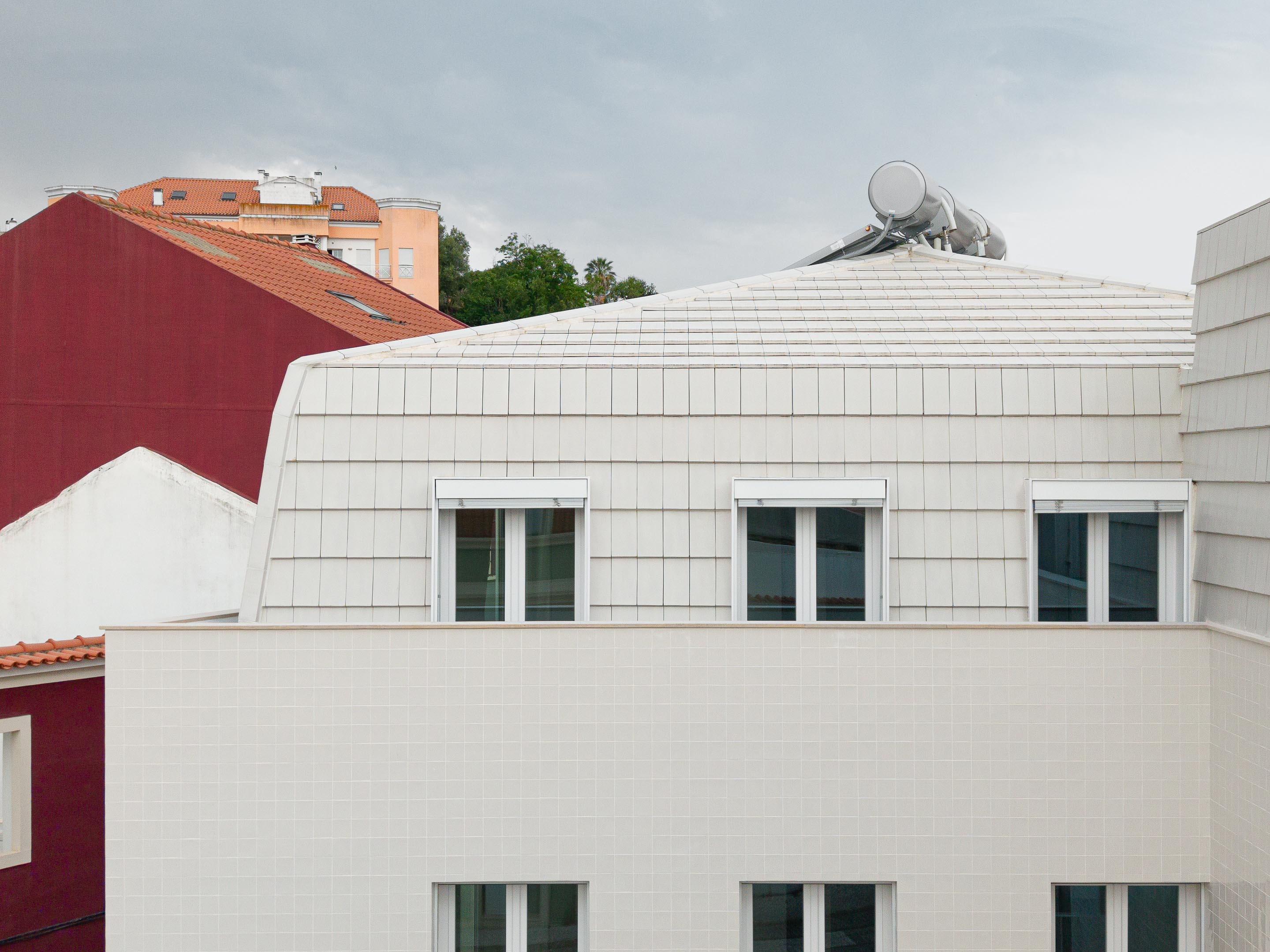 Fachada com revestimento em azulejo branco e cobertura amansardada em telha plana branca. Vãos com caixilharia de PVC branca — Edifício Actriz Virginia arquitectura Adarq – André David Arquitecto fotografia Ivo Tavares