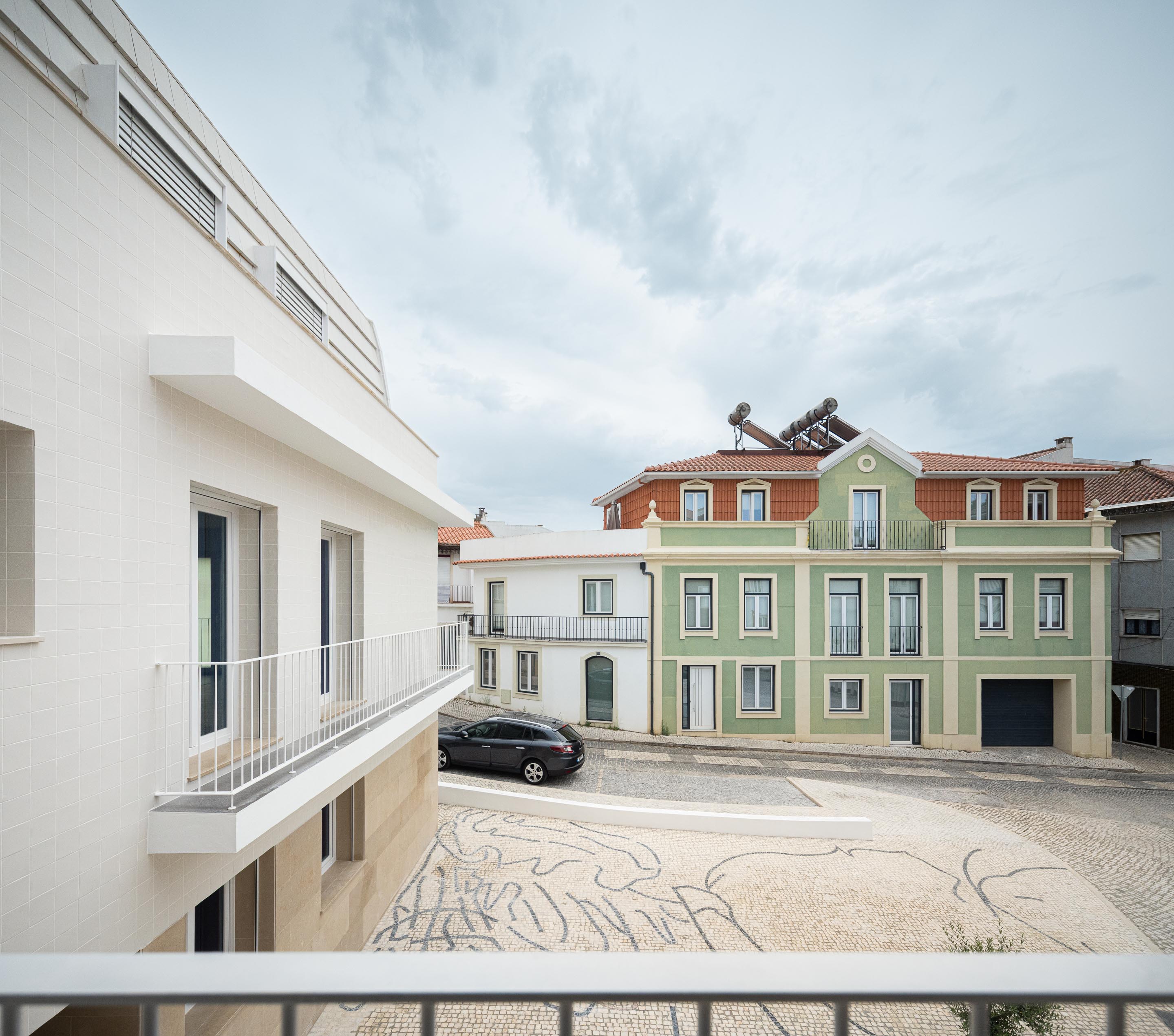 Varanda com guarda-corpos branco, fachada em azulejo branco e base em pedra calcária. Pavimento em calçada portuguesa e edifícios tradicionais — Edifício Actriz Virginia arquitectura Adarq – André David Arquitecto fotografia Ivo Tavares