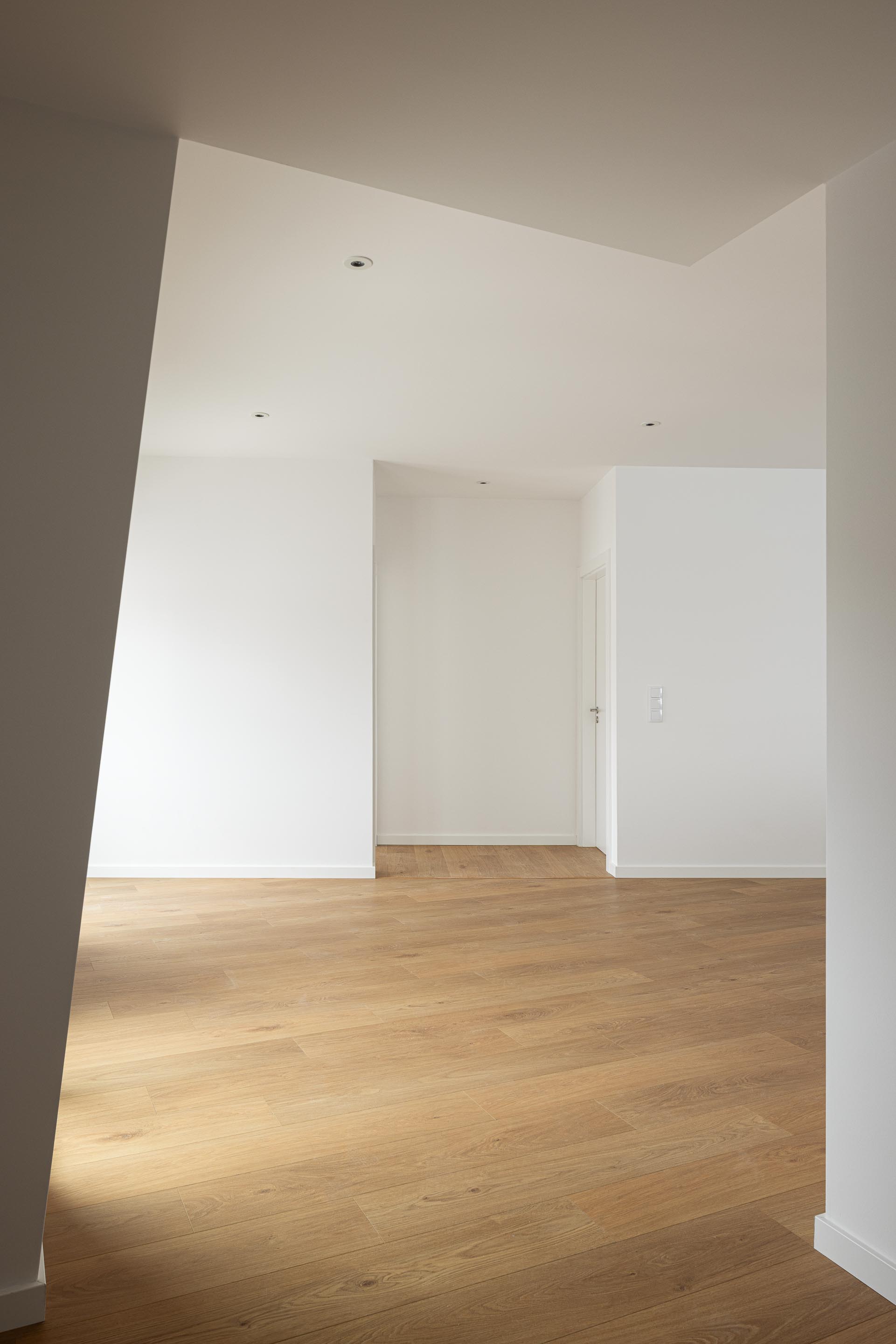 Interior de sala com pavimento em madeira de carvalho clara e paredes brancas. Iluminação embutida no teto — Edifício Actriz Virginia arquitectura Adarq – André David Arquitecto fotografia Ivo Tavares