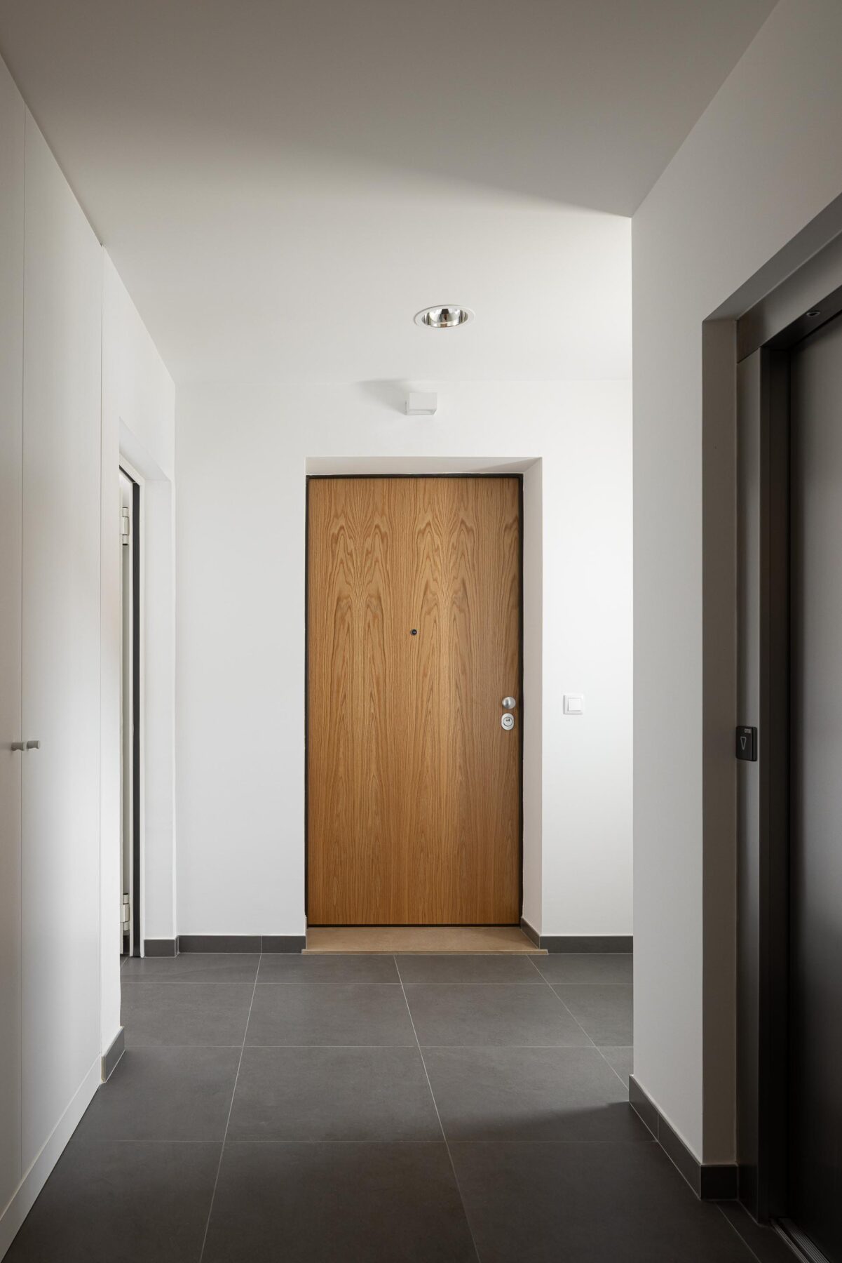 Corredor com pavimento em cerâmica cinzenta e paredes brancas. Porta de entrada em madeira de carvalho — Edifício Actriz Virginia arquitectura Adarq – André David Arquitecto fotografia Ivo Tavares