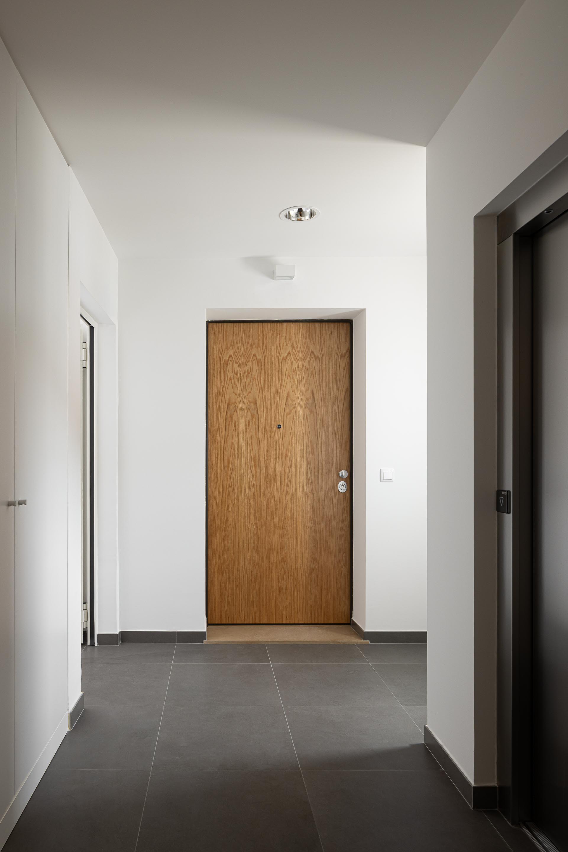 Corredor com pavimento em cerâmica cinzenta e paredes brancas. Porta de entrada em madeira de carvalho — Edifício Actriz Virginia arquitectura Adarq – André David Arquitecto fotografia Ivo Tavares