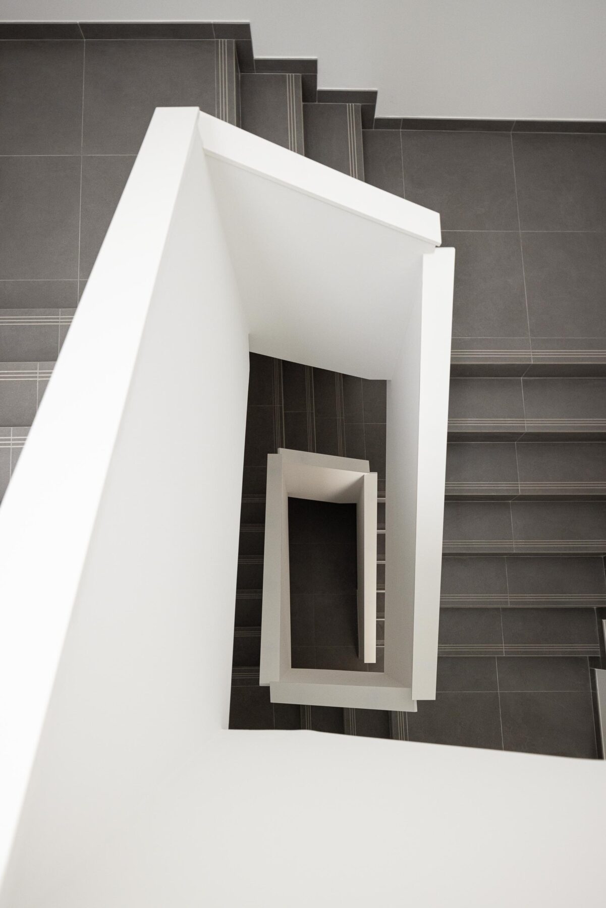 Escada com guardas brancas geométricas e pavimento em cerâmica cinzenta. Perspetiva vertical — Edifício Actriz Virginia arquitectura Adarq – André David Arquitecto fotografia Ivo Tavares