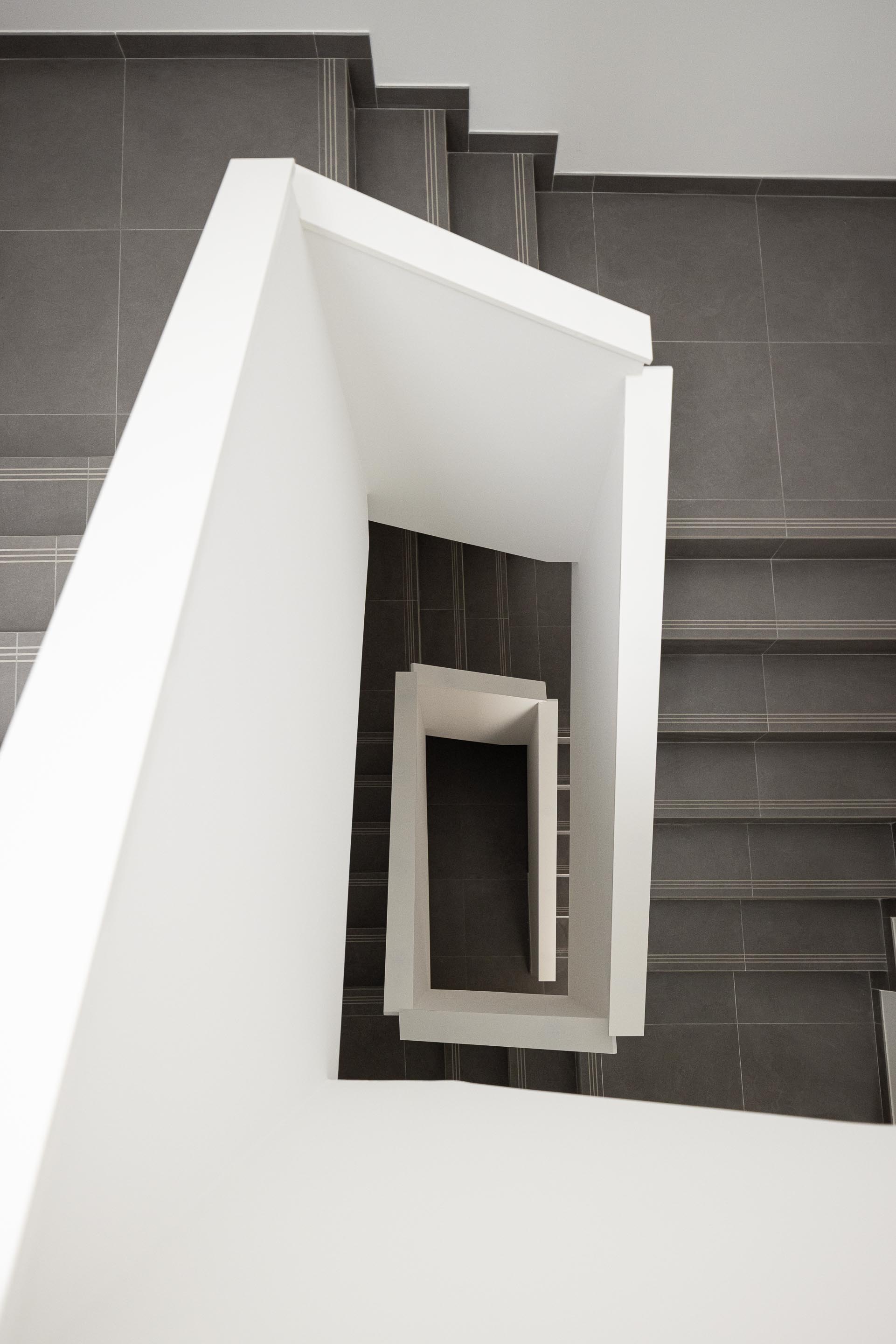 Escada com guardas brancas geométricas e pavimento em cerâmica cinzenta. Perspetiva vertical — Edifício Actriz Virginia arquitectura Adarq – André David Arquitecto fotografia Ivo Tavares