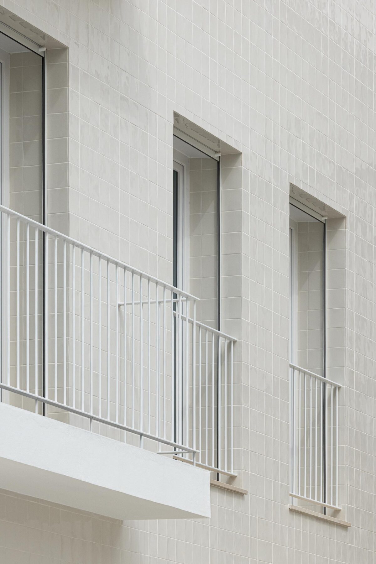 Pormenor da fachada em azulejo branco com textura e guarda-corpos metálicos brancos nos vãos — Edifício Actriz Virginia arquitectura Adarq – André David Arquitecto fotografia Ivo Tavares