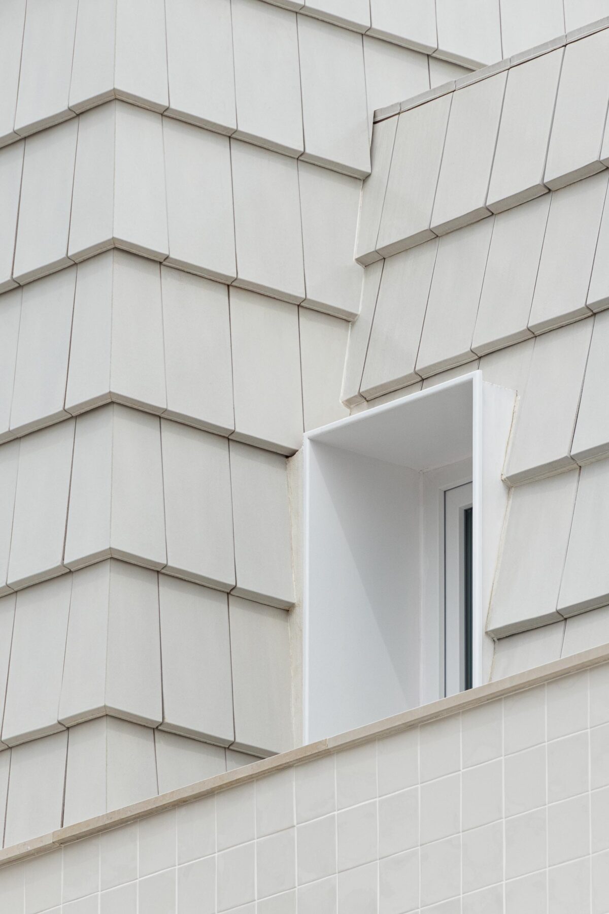 Detalhe da transição entre a fachada em azulejo branco e a cobertura amansardada em telha plana branca. Vão recuado — Edifício Actriz Virginia arquitectura Adarq – André David Arquitecto fotografia Ivo Tavares