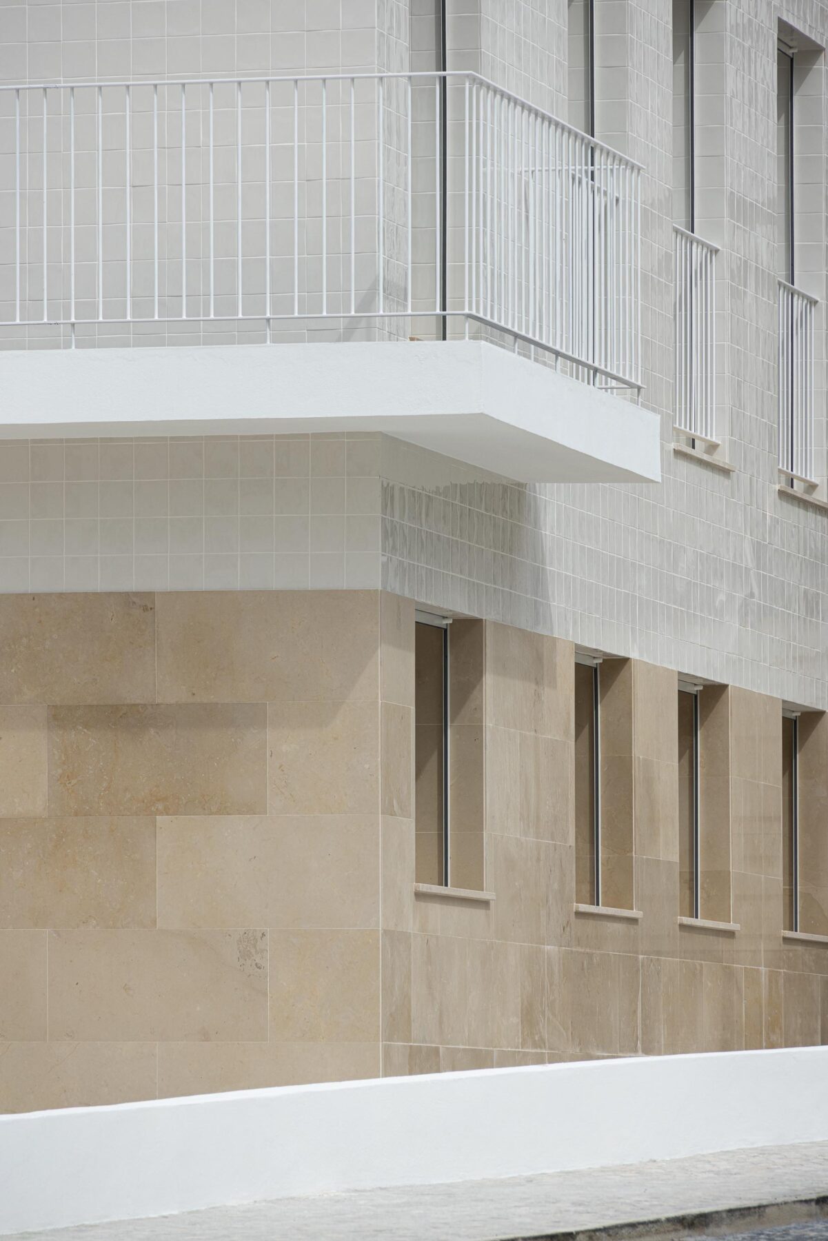 Fachada com embasamento em pedra calcária e revestimento superior em azulejo branco. Varanda branca em consola — Edifício Actriz Virginia arquitectura Adarq – André David Arquitecto fotografia Ivo Tavares