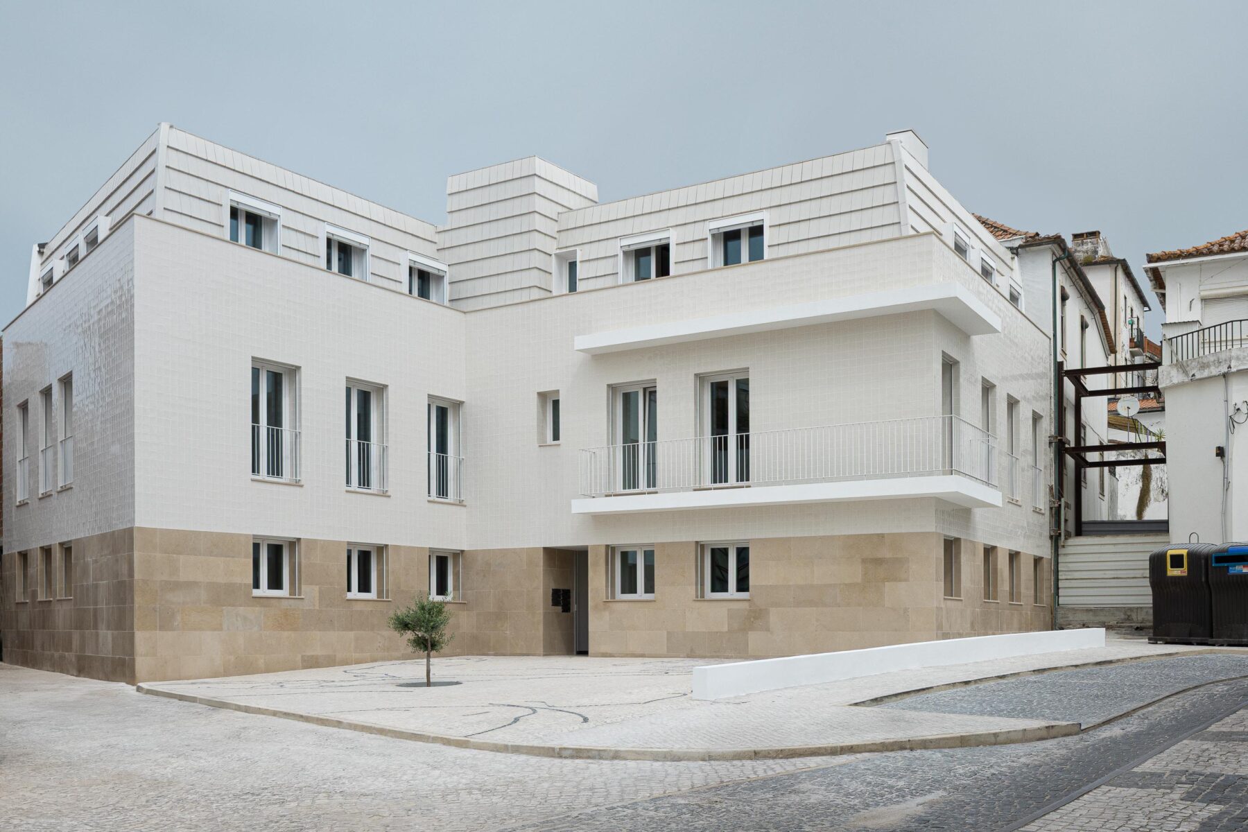 Edifício com volumetria em L, base em pedra calcária e fachada em azulejo branco. Cobertura amansardada e calçada portuguesa — Edifício Actriz Virginia arquitectura Adarq – André David Arquitecto fotografia Ivo Tavares