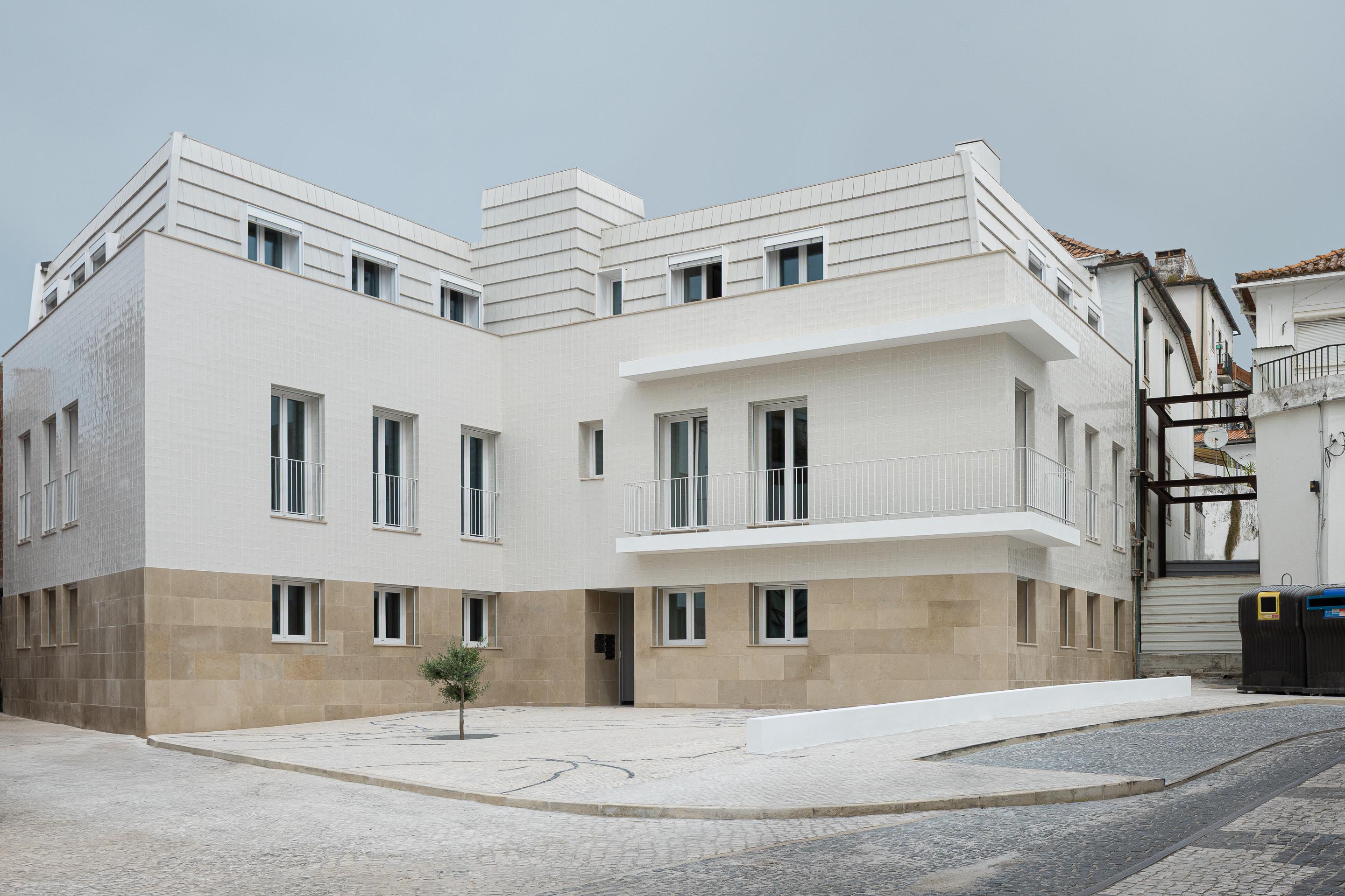 Edifício com volumetria em L, base em pedra calcária e fachada em azulejo branco. Cobertura amansardada e calçada portuguesa — Edifício Actriz Virginia arquitectura Adarq – André David Arquitecto fotografia Ivo Tavares
