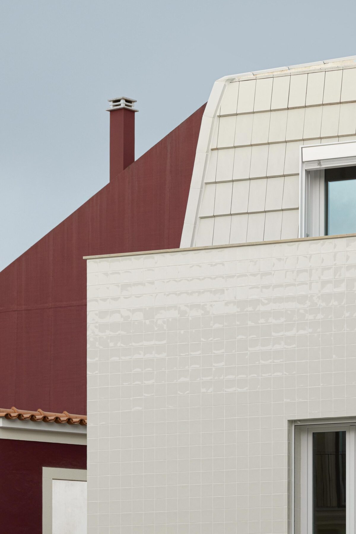 Fachada em azulejo branco e cobertura amansardada em telha plana, contrastando com a empena vermelha do edifício adjacente — Edifício Actriz Virginia arquitectura Adarq – André David Arquitecto fotografia Ivo Tavares