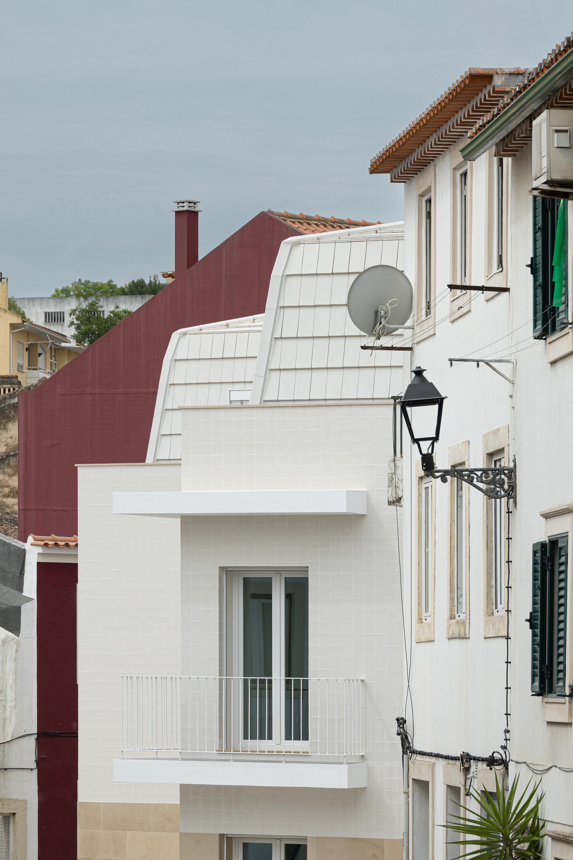 Fachada em azulejo branco e base em pedra calcária, com cobertura amansardada. Integração no contexto urbano tradicional — Edifício Actriz Virginia arquitectura Adarq – André David Arquitecto fotografia Ivo Tavares