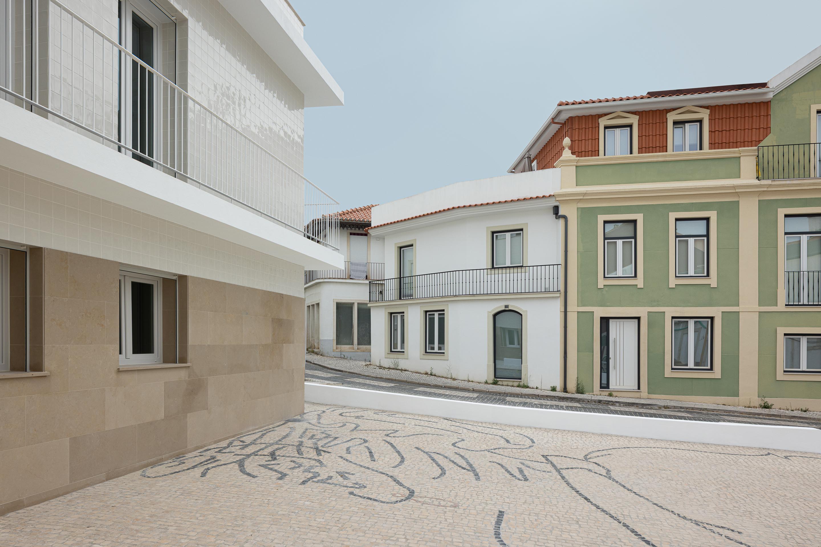 Pavimento em calçada portuguesa com desenho, base do edifício em pedra calcária e fachada em azulejo branco. Contexto urbano — Edifício Actriz Virginia arquitectura Adarq – André David Arquitecto fotografia Ivo Tavares