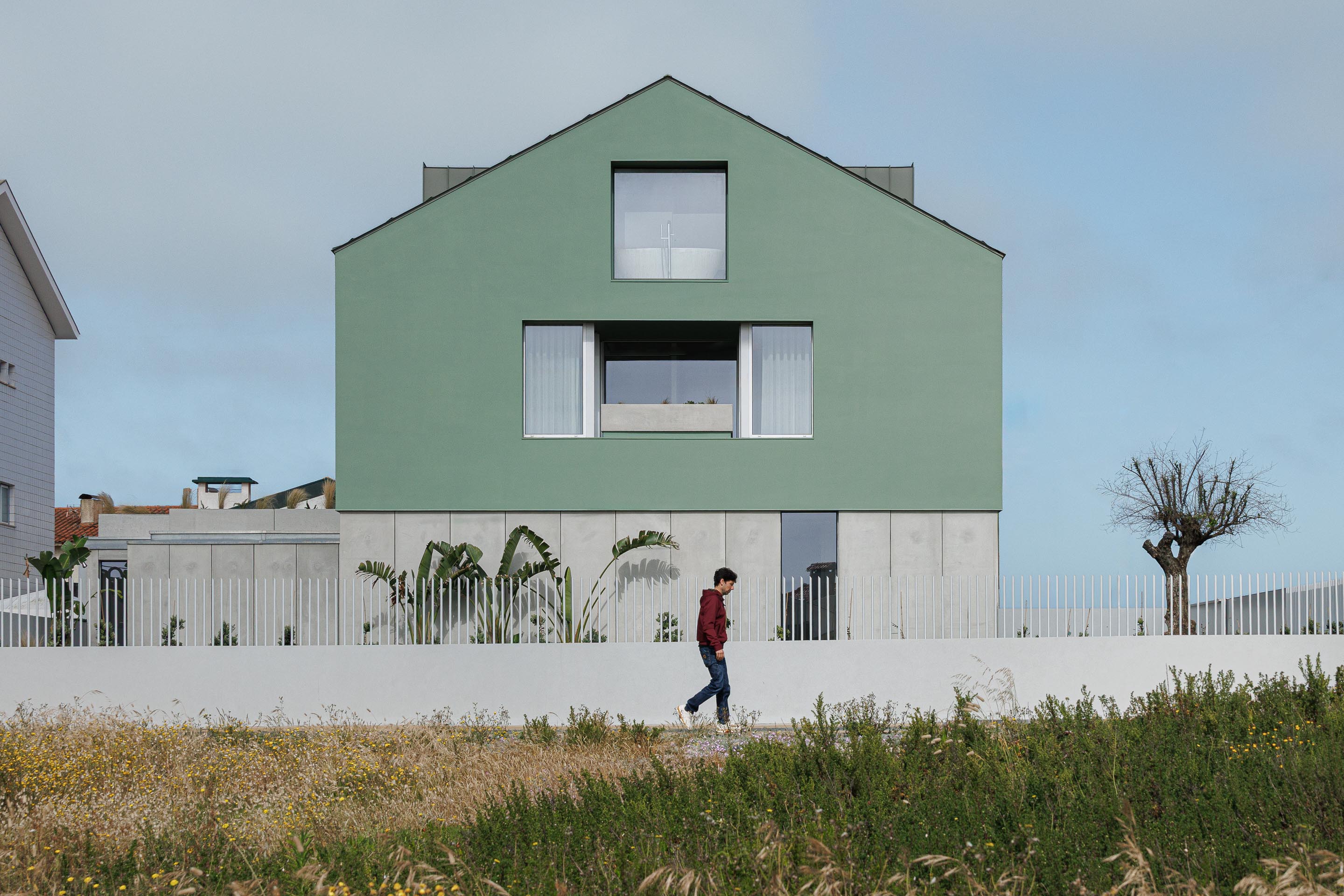 Fachada principal da moradia verde com cobertura de duas águas, embasamento em betão e vedação branca, integrada na paisagem — Casa Verde arquitectura M2 Senos Arquitectos fotografia Ivo Tavares