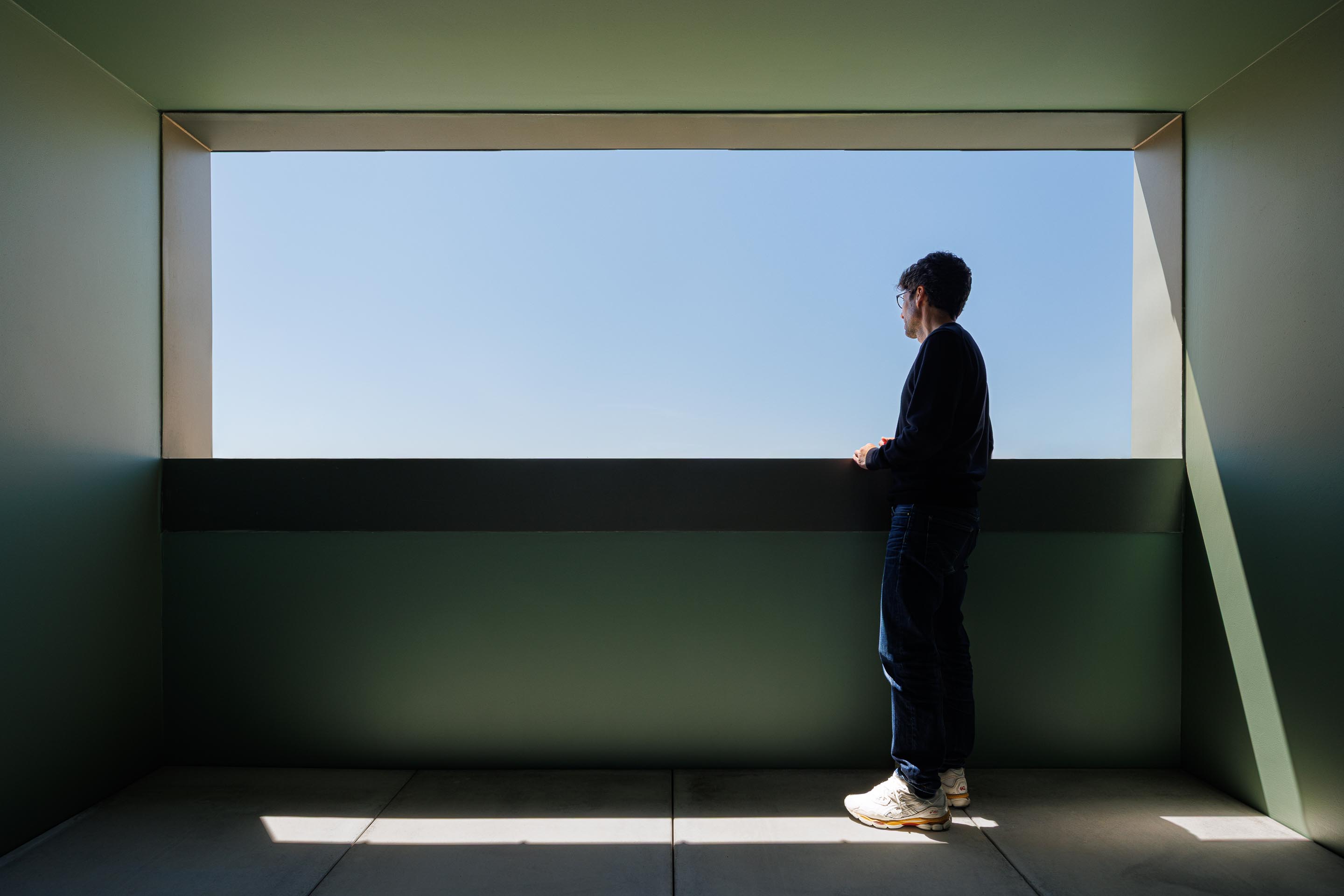 Interior da mansarda com paredes verdes, pavimento em betão e grande vão horizontal que enquadra a paisagem exterior — Casa Verde arquitectura M2 Senos Arquitectos fotografia Ivo Tavares