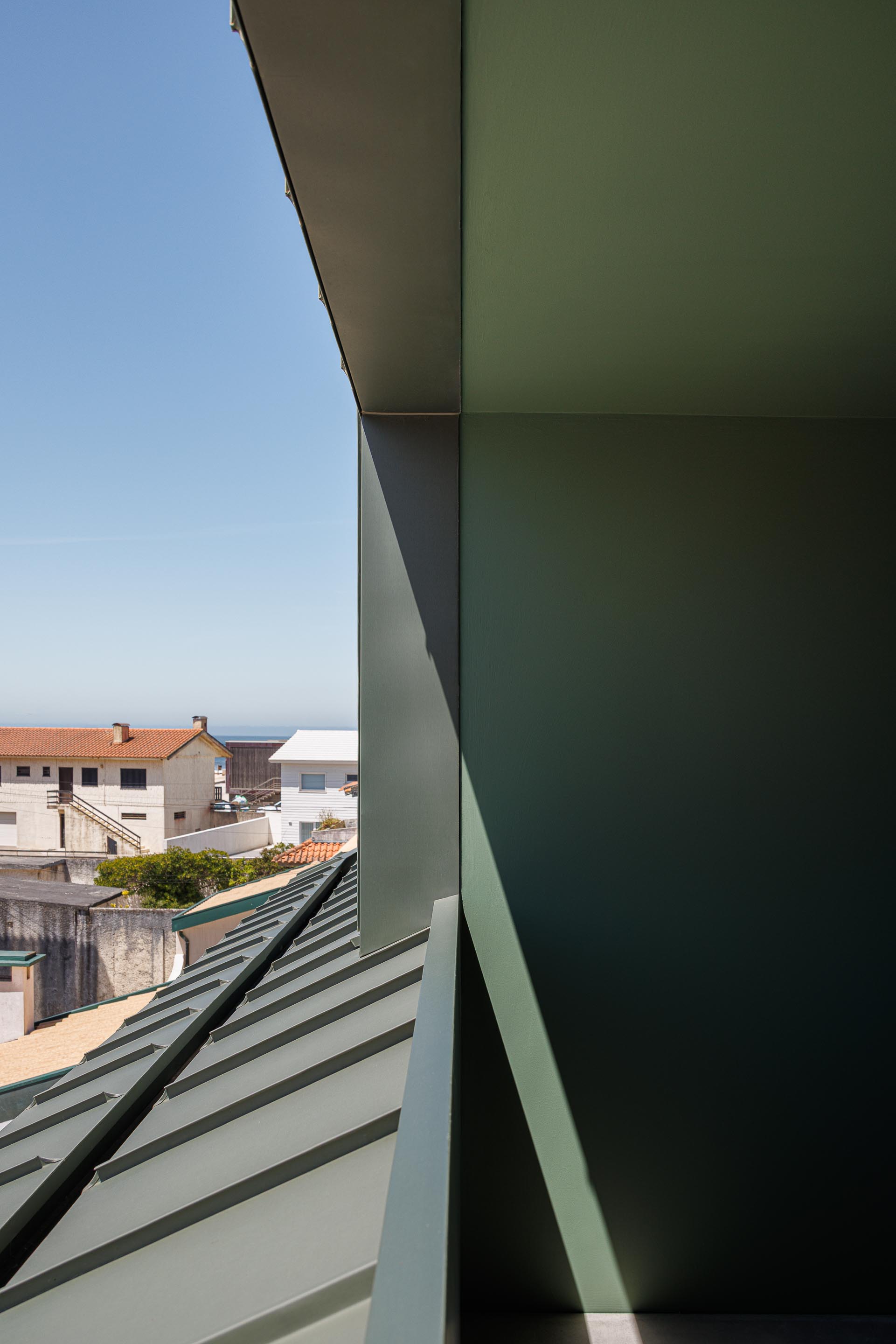 Vista exterior da mansarda verde, mostrando a cobertura inclinada em zinco e o casario envolvente sob luz solar — Casa Verde arquitectura M2 Senos Arquitectos fotografia Ivo Tavares