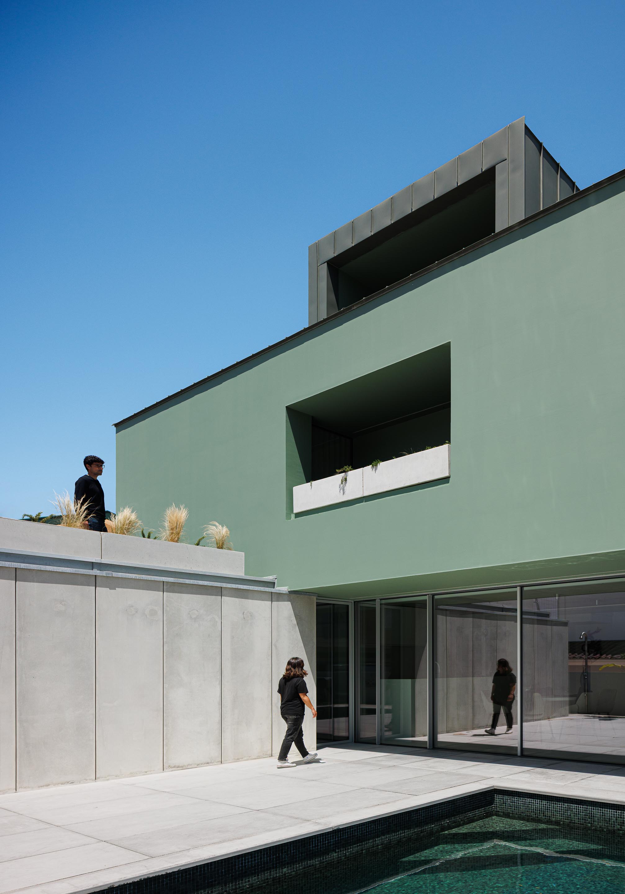 Logradouro exterior com piscina de cor escura, pavimento em lajetas claras e fachada com grandes vãos envidraçados — Casa Verde arquitectura M2 Senos Arquitectos fotografia Ivo Tavares