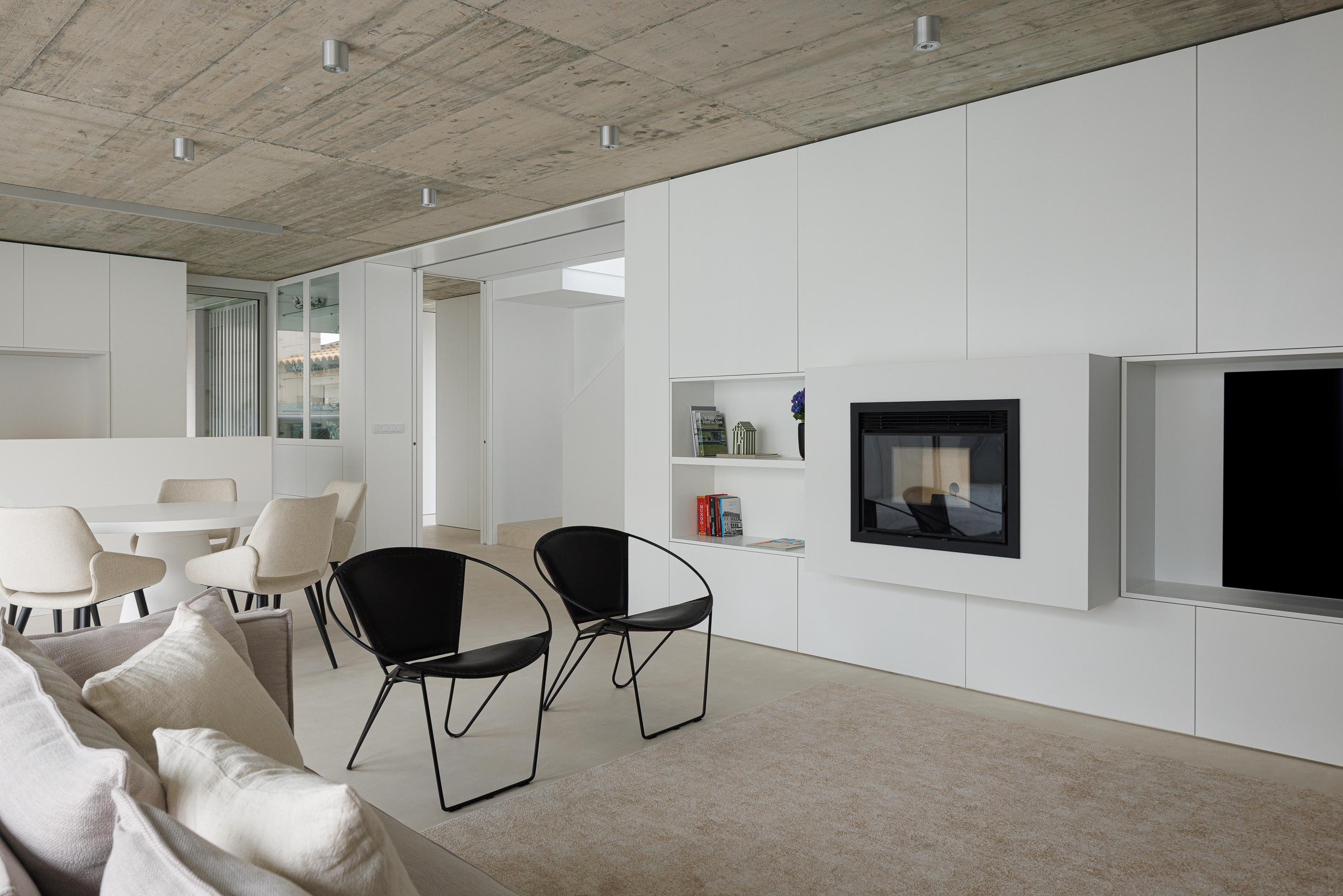 Interior da sala de estar e jantar com tecto em betão aparente, pavimento claro e mobiliário branco minimalista — Casa Verde arquitectura M2 Senos Arquitectos fotografia Ivo Tavares