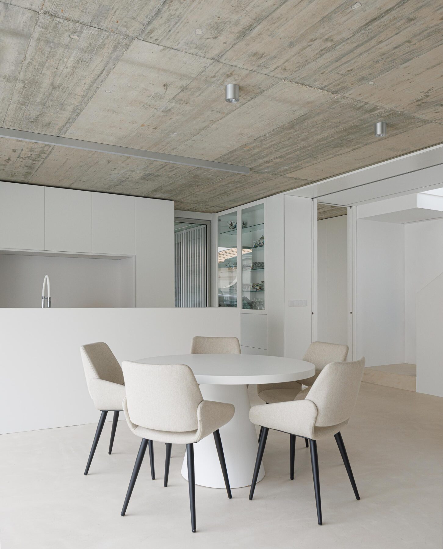 Espaço de refeições com mesa redonda branca, cadeiras estofadas e tecto em betão aparente, integrado na cozinha — Casa Verde arquitectura M2 Senos Arquitectos fotografia Ivo Tavares