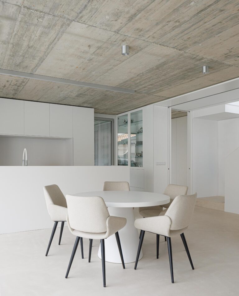 Espaço de refeições com mesa redonda branca, cadeiras estofadas e tecto em betão aparente, integrado na cozinha — Casa Verde arquitectura M2 Senos Arquitectos fotografia Ivo Tavares