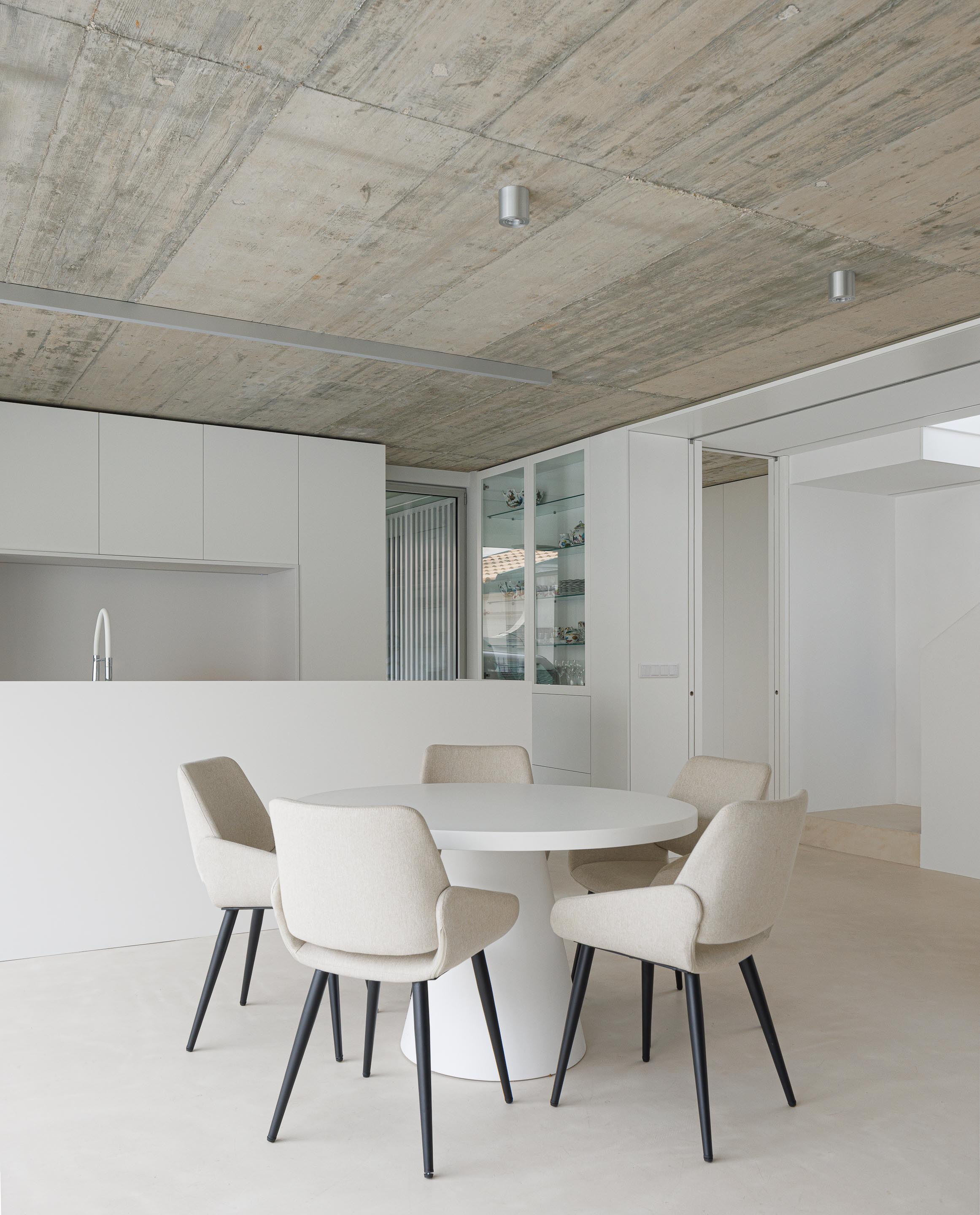 Espaço de refeições com mesa redonda branca, cadeiras estofadas e tecto em betão aparente, integrado na cozinha — Casa Verde arquitectura M2 Senos Arquitectos fotografia Ivo Tavares
