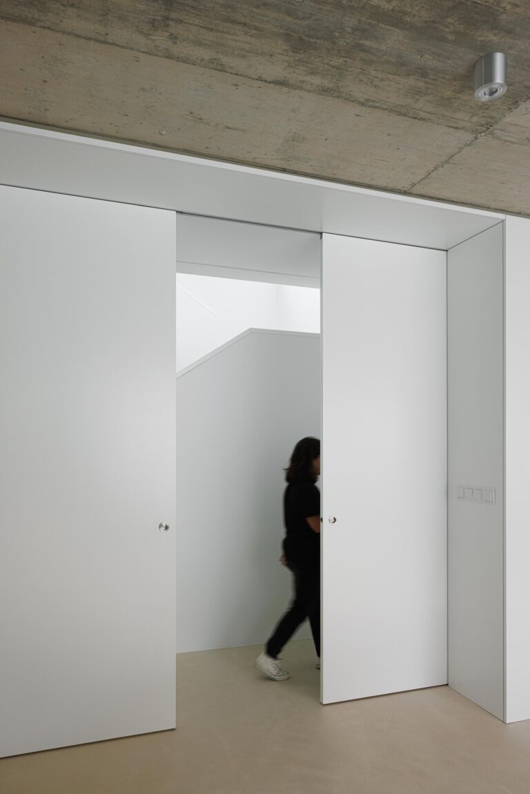 Corredor de transição com paredes brancas, portas de correr e tecto em betão aparente, criando um espaço depurado — Casa Verde arquitectura M2 Senos Arquitectos fotografia Ivo Tavares