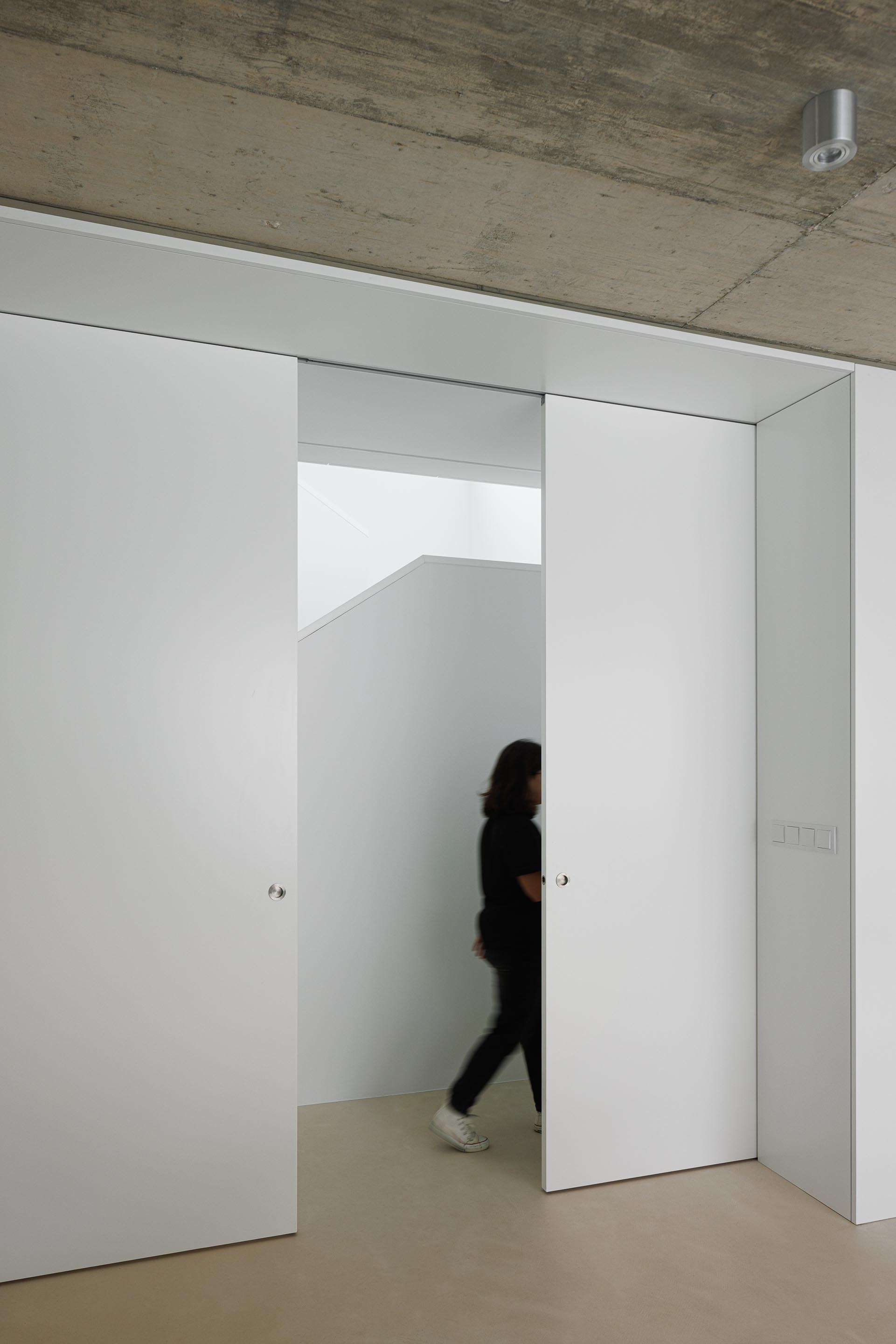 Corredor de transição com paredes brancas, portas de correr e tecto em betão aparente, criando um espaço depurado — Casa Verde arquitectura M2 Senos Arquitectos fotografia Ivo Tavares