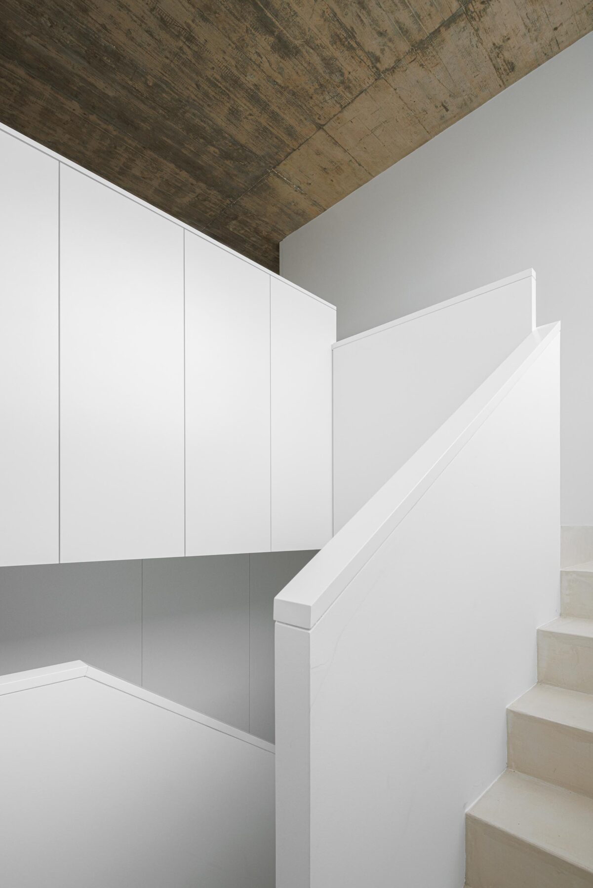 Escada de pavimento claro com paredes e armários brancos, sob um tecto em betão aparente, criando um contraste material — Casa Verde arquitectura M2 Senos Arquitectos fotografia Ivo Tavares