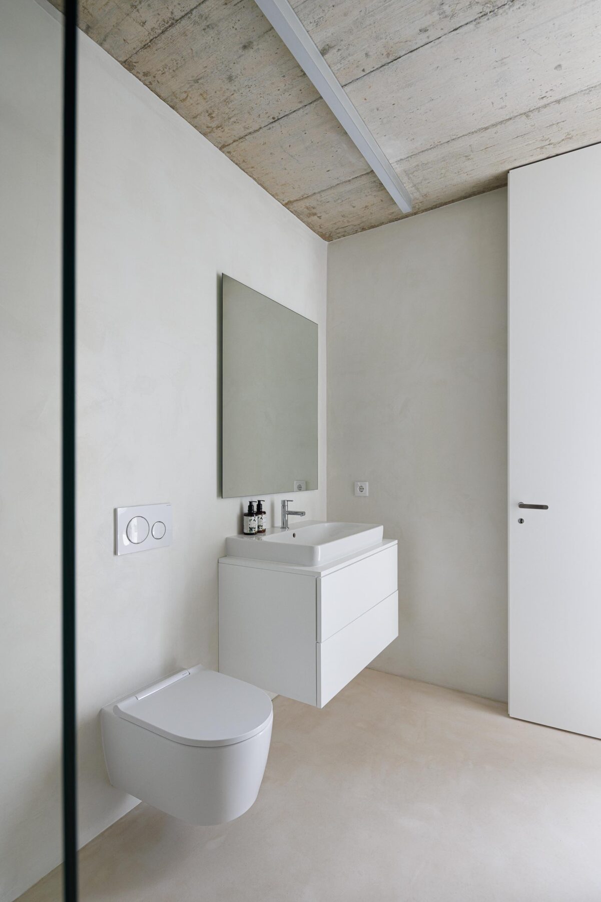 Interior da casa de banho com lavatório suspenso branco, sanita e espelho, sob um tecto em betão aparente — Casa Verde arquitectura M2 Senos Arquitectos fotografia Ivo Tavares