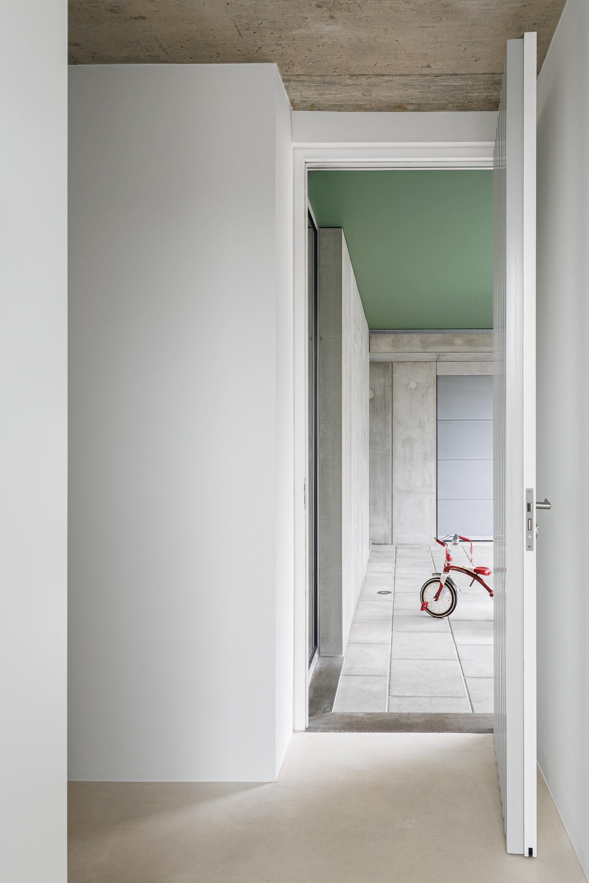 Vão de porta com vista para um espaço de pavimento em lajetas, paredes em betão aparente e tecto verde — Casa Verde arquitectura M2 Senos Arquitectos fotografia Ivo Tavares
