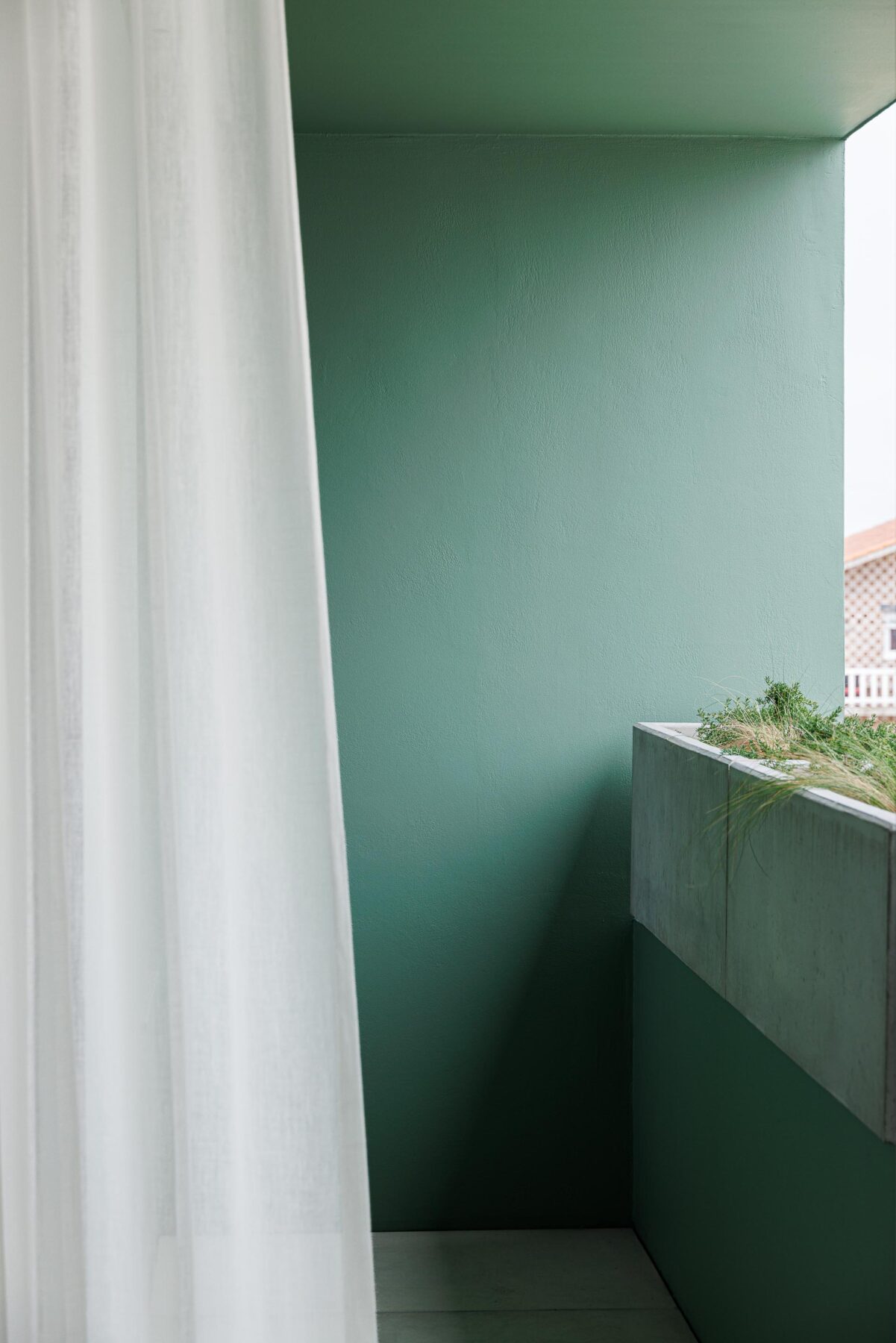 Detalhe da varanda com parede verde, floreira em betão aparente e cortina branca translúcida — Casa Verde arquitectura M2 Senos Arquitectos fotografia Ivo Tavares