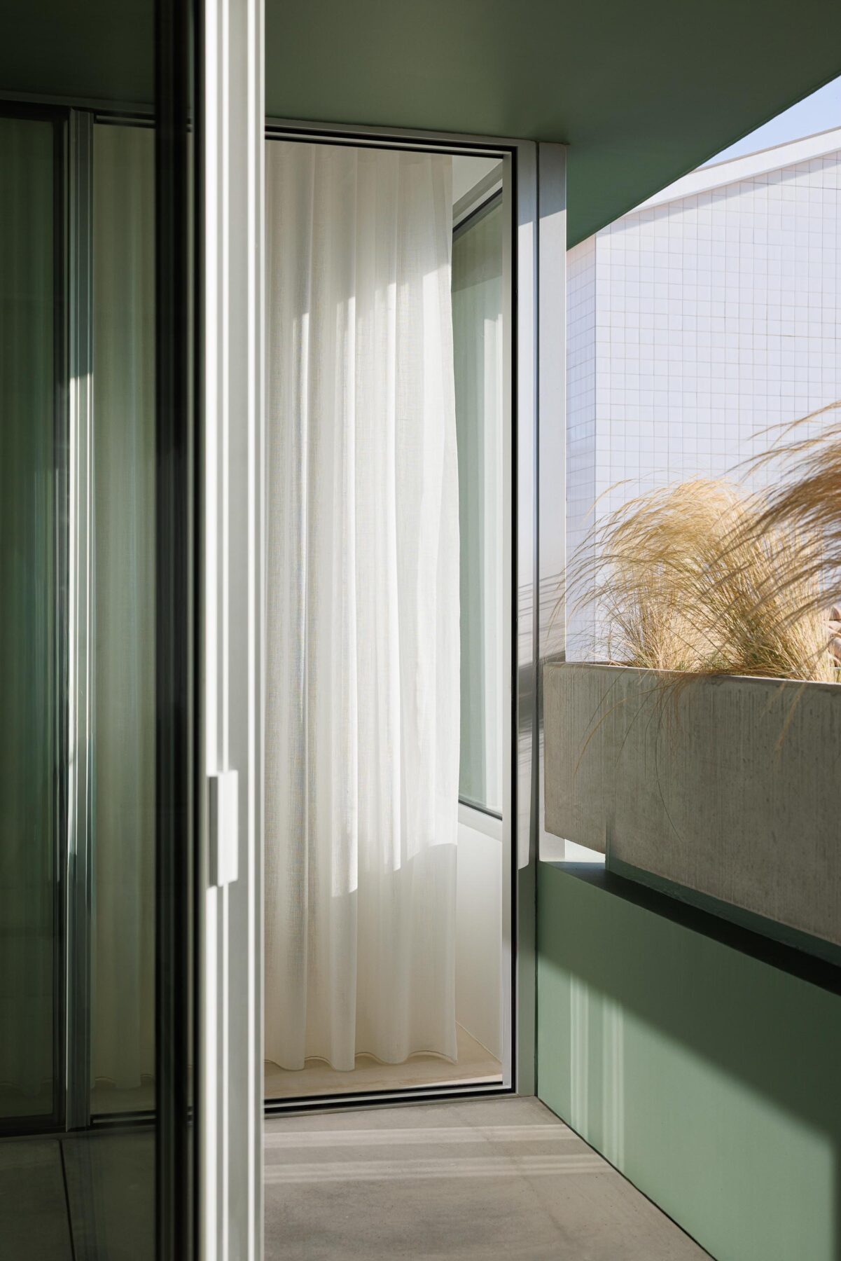 Varanda com cortina branca, floreira em betão aparente e parede verde, oferecendo uma vista para o exterior — Casa Verde arquitectura M2 Senos Arquitectos fotografia Ivo Tavares