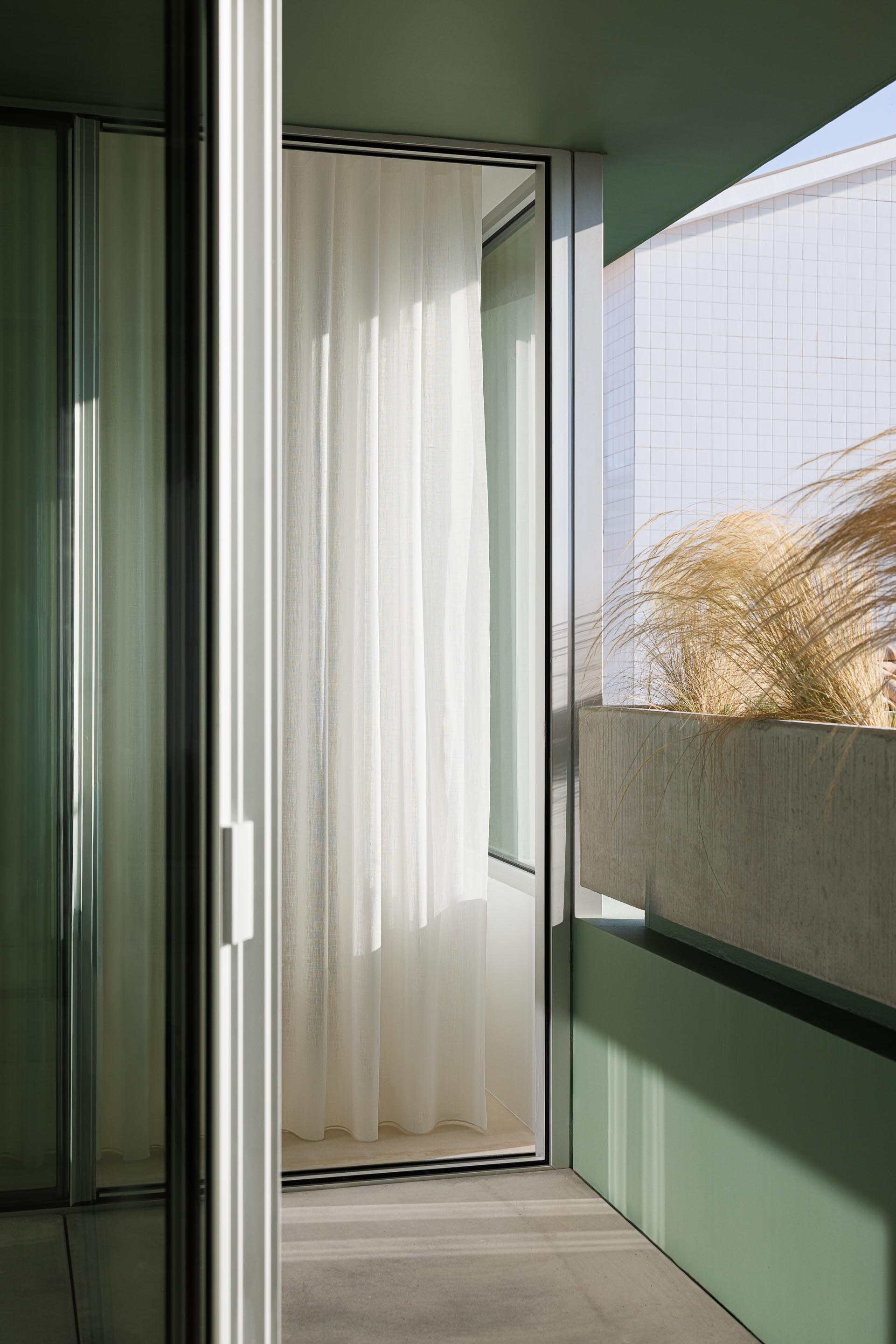 Varanda com cortina branca, floreira em betão aparente e parede verde, oferecendo uma vista para o exterior — Casa Verde arquitectura M2 Senos Arquitectos fotografia Ivo Tavares