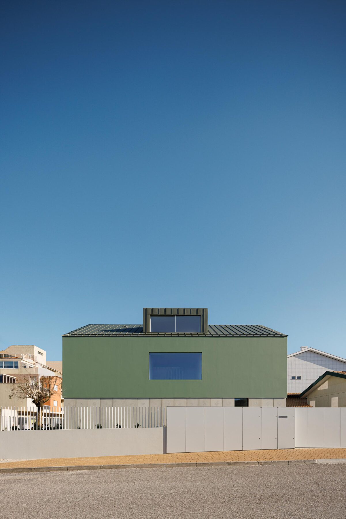 Fachada principal da moradia de volume compacto verde, com cobertura inclinada e mansarda, sobre embasamento em betão — Casa Verde arquitectura M2 Senos Arquitectos fotografia Ivo Tavares