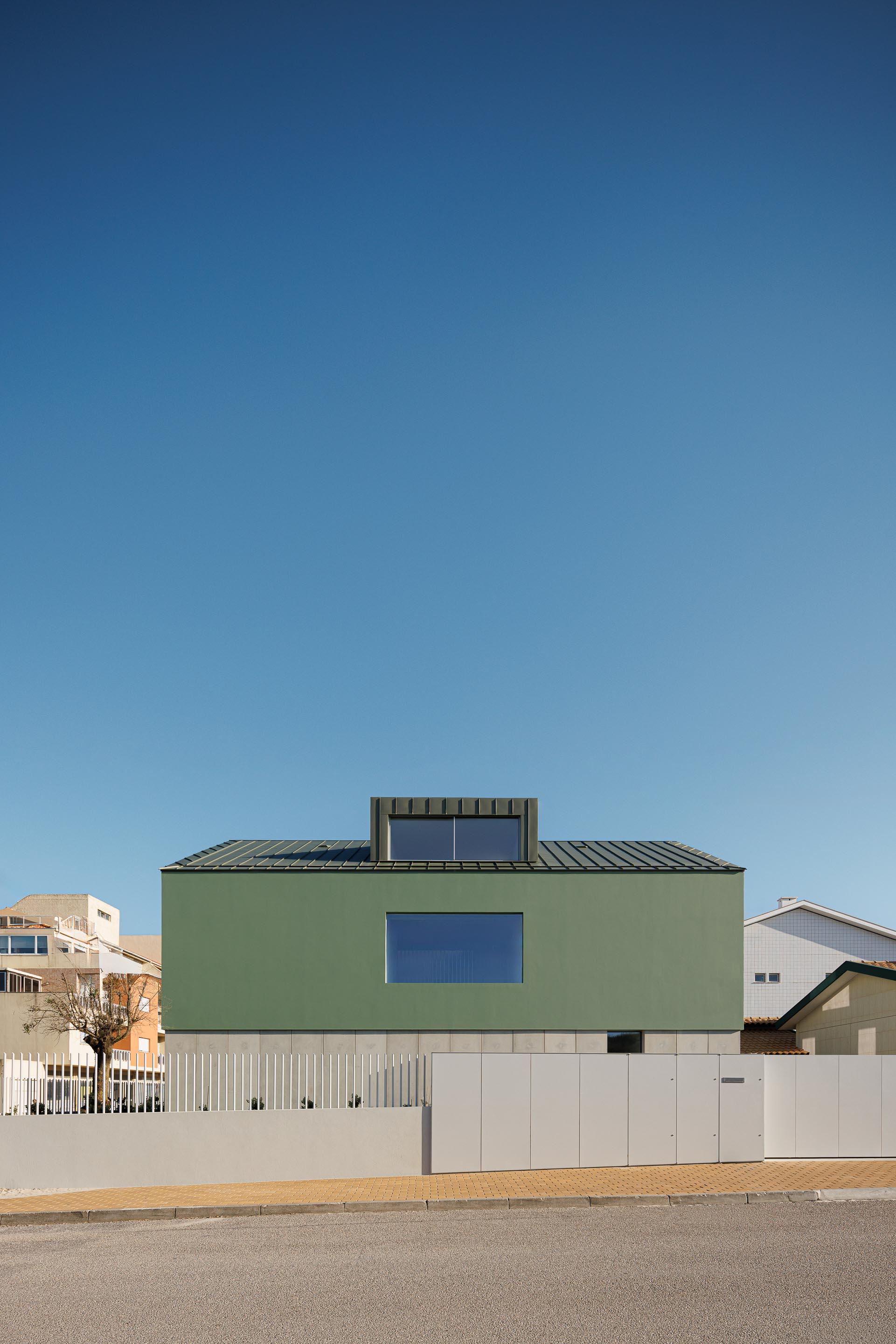 Fachada principal da moradia de volume compacto verde, com cobertura inclinada e mansarda, sobre embasamento em betão — Casa Verde arquitectura M2 Senos Arquitectos fotografia Ivo Tavares