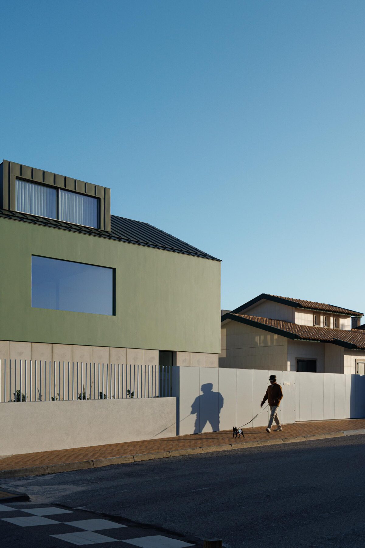 Moradia de volume compacto verde com cobertura inclinada e mansarda, sobre embasamento em betão, vista da rua — Casa Verde arquitectura M2 Senos Arquitectos fotografia Ivo Tavares