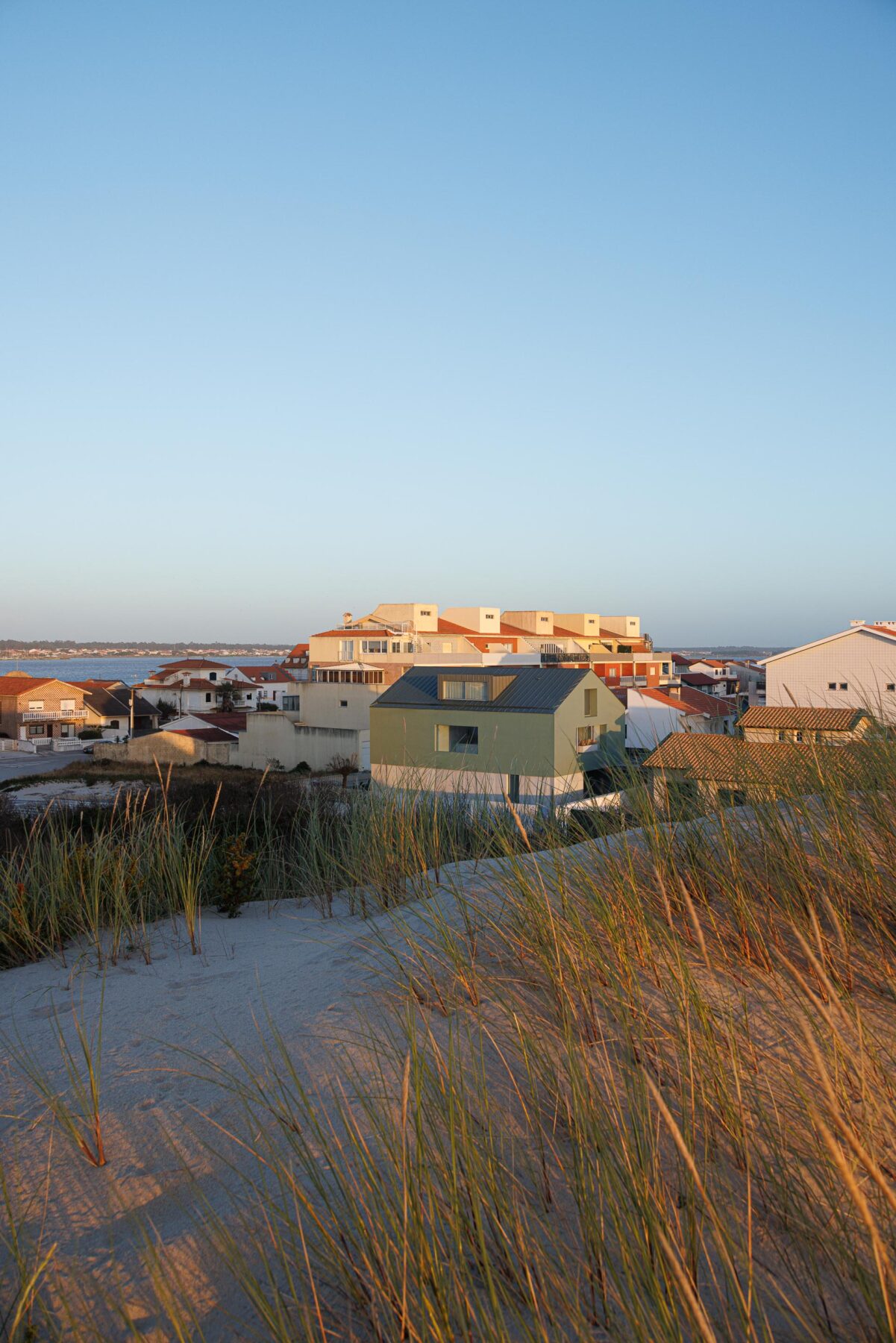 Vista da moradia verde a partir da duna, mostrando a sua integração na paisagem e o oceano ao fundo — Casa Verde arquitectura M2 Senos Arquitectos fotografia Ivo Tavares