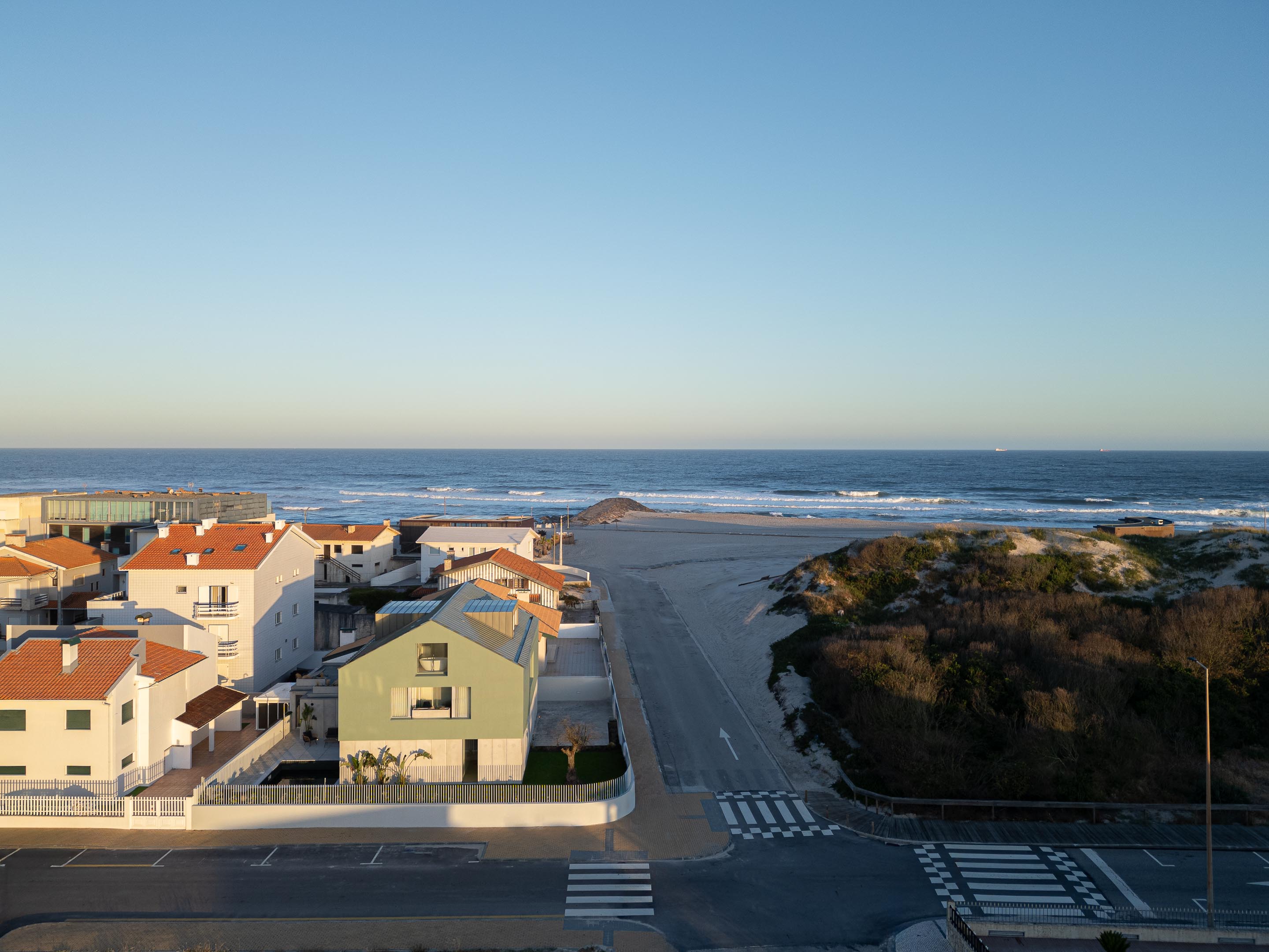 Vista aérea da moradia verde, revelando a sua implantação entre o casario, a praia e o vasto oceano — Casa Verde arquitectura M2 Senos Arquitectos fotografia Ivo Tavares