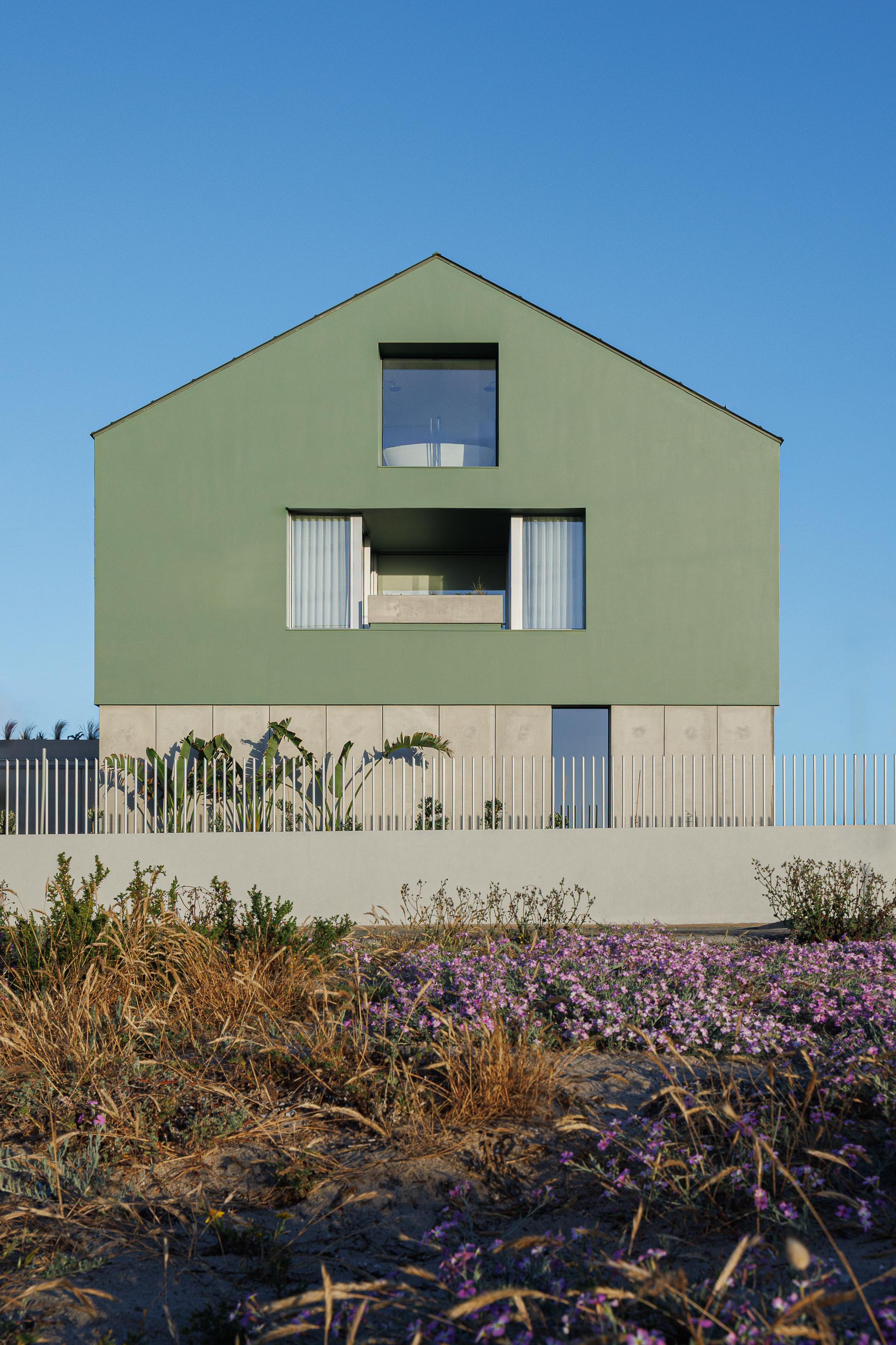 Fachada principal da moradia verde com cobertura inclinada e mansarda, sobre embasamento em betão, junto à duna — Casa Verde arquitectura M2 Senos Arquitectos fotografia Ivo Tavares