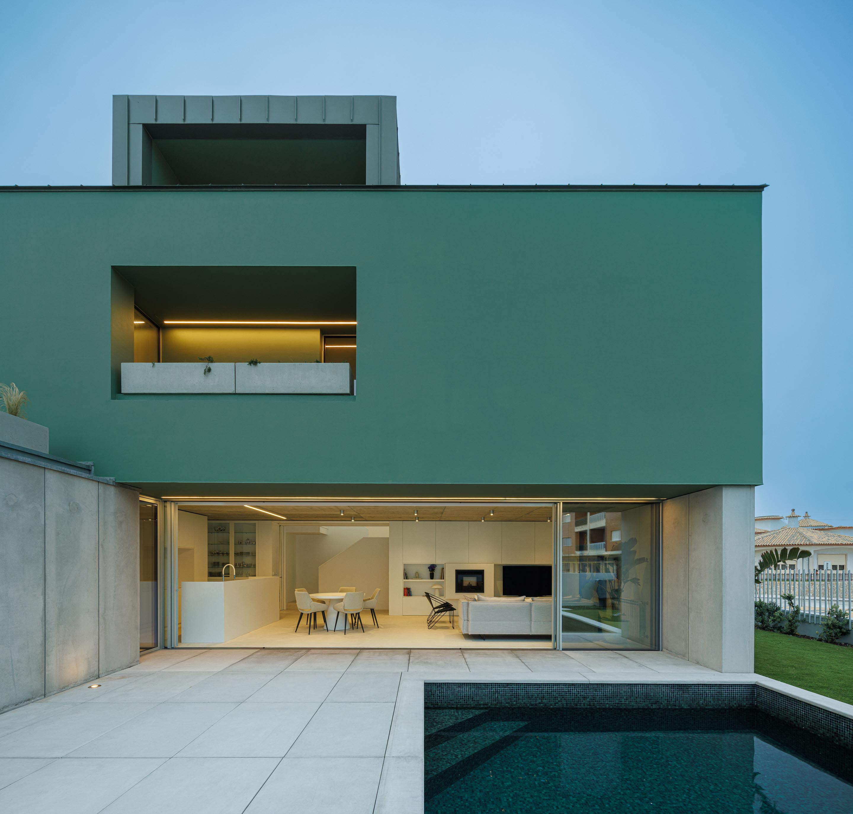 Logradouro exterior com piscina e fachada verde iluminada, revelando a continuidade interior-exterior ao entardecer — Casa Verde arquitectura M2 Senos Arquitectos fotografia Ivo Tavares